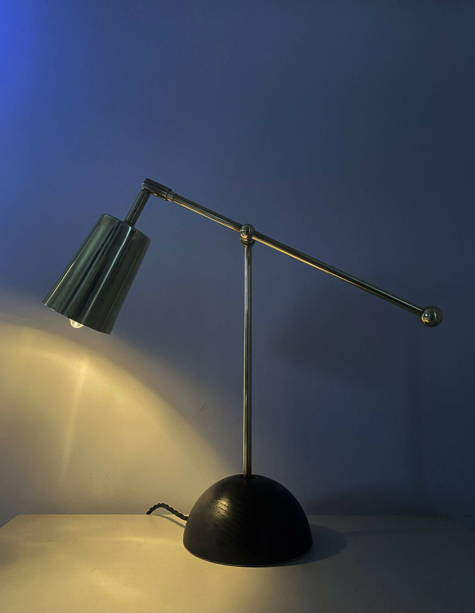 An elegant brass desk lamp with a hand turned solid oak base and a hand polished brass finish, positioned against a neutral background,  available  to buy on the-salon.com. SALON curates the finest , unique, handmade pieces from the interior industry's best makers and brands. Shop luxury furniture, lighting, rugs, art, antiques and vintage pieces and accessories from SALON interior designed rooms.