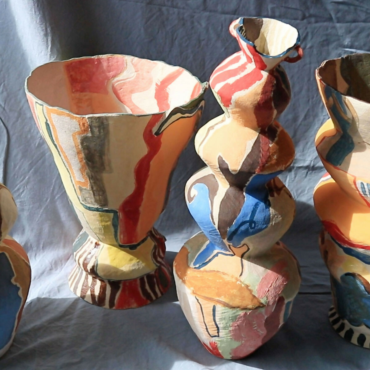 Colorful ceramic vases with abstract designs on a blue cloth background, available  to buy on the-salon.com. SALON curates the finest , unique, handmade pieces from the interior industry's best makers and brands. Shop luxury furniture, lighting, rugs, art, antiques and vintage pieces and accessories from SALON interior designed rooms.