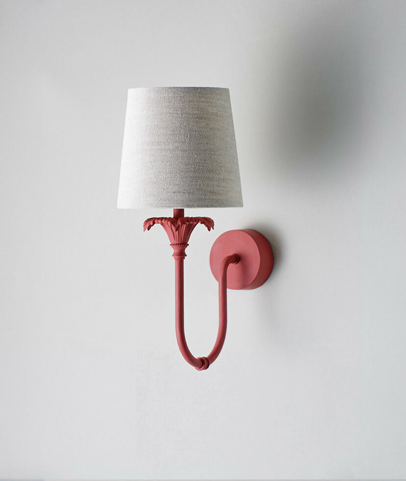 A wall-mounted light fixture with a red-colored metal arm and a white, solid-patterned lampshade,  available  to buy on the-salon.com. SALON curates the finest , unique, handmade pieces from the interior industry's best makers and brands. Shop luxury furniture, lighting, rugs, art, antiques and vintage pieces and accessories from SALON interior designed rooms.