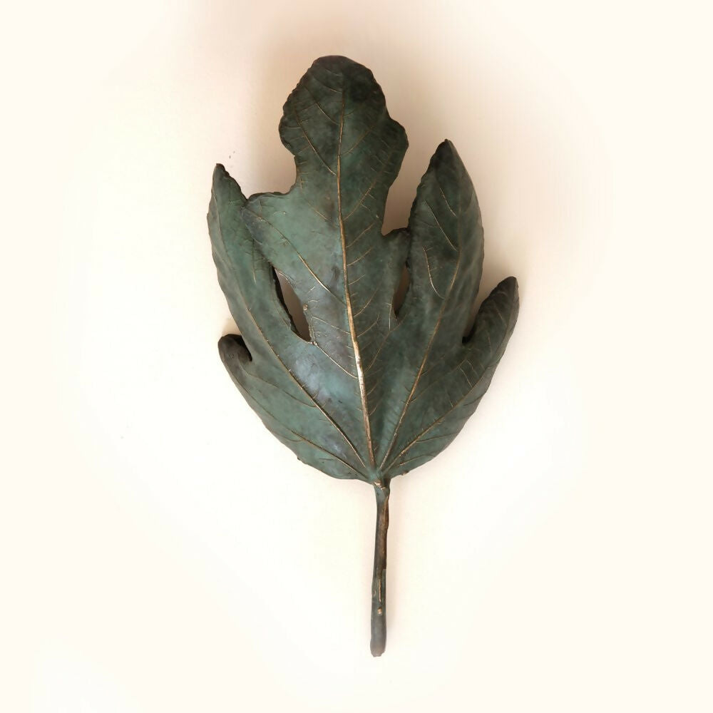 A bronze wall light fixture designed to resemble a fig leaf, with a textured surface and a wall mounting bracket,  available  to buy on the-salon.com. SALON curates the finest , unique, handmade pieces from the interior industry's best makers and brands. Shop luxury furniture, lighting, rugs, art, antiques and vintage pieces and accessories from SALON interior designed rooms.