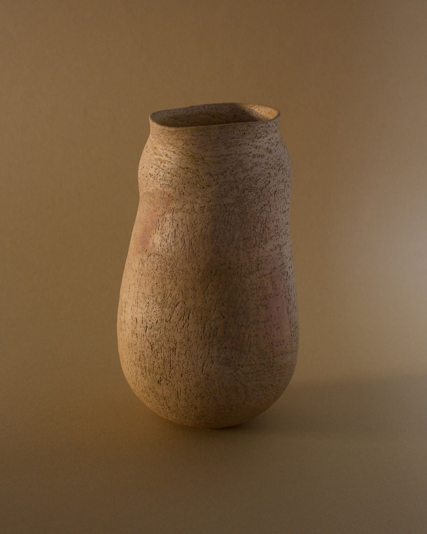 A brown ceramic vase with an organic, irregular silhouette, featuring a smooth yet textured surface with subtle flashes of burnt orange,  available  to buy on the-salon.com. SALON curates the finest , unique, handmade pieces from the interior industry's best makers and brands. Shop luxury furniture, lighting, rugs, art, antiques and vintage pieces and accessories from SALON interior designed rooms.