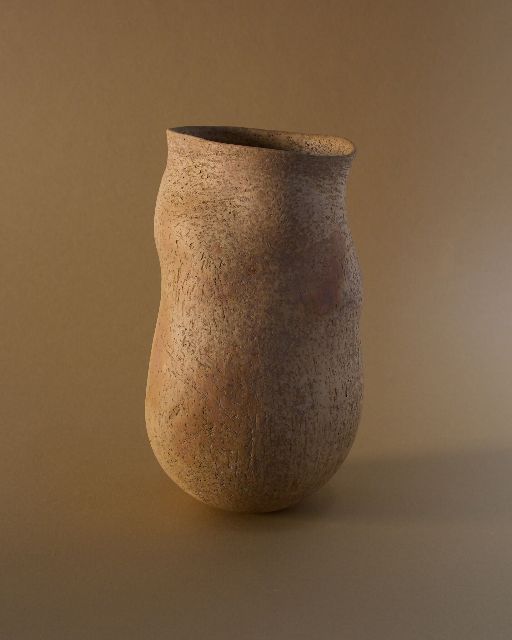 A brown ceramic vase with an organic, irregular silhouette, featuring a smooth yet textured surface with subtle flashes of burnt orange,  available  to buy on the-salon.com. SALON curates the finest , unique, handmade pieces from the interior industry's best makers and brands. Shop luxury furniture, lighting, rugs, art, antiques and vintage pieces and accessories from SALON interior designed rooms.