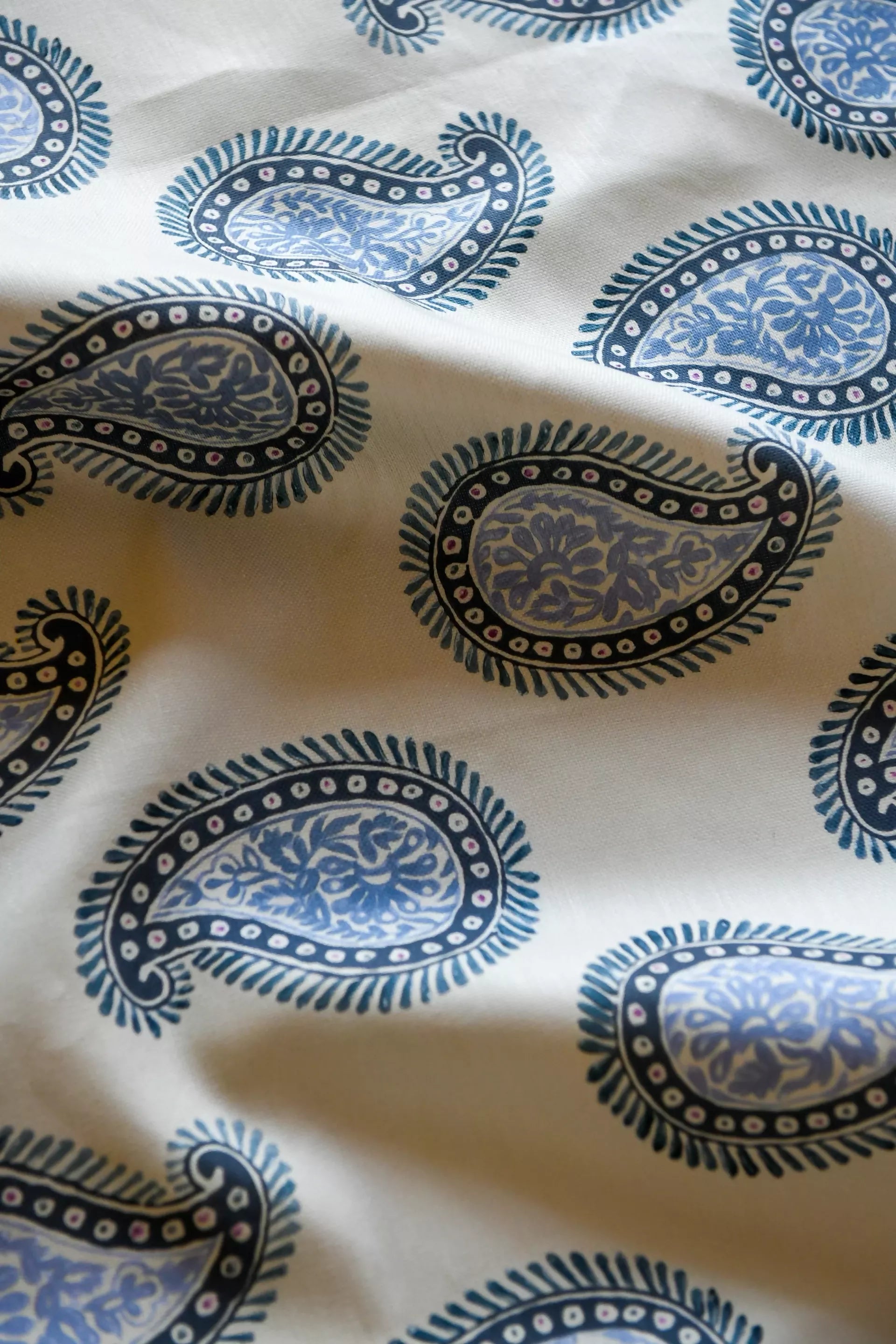 Close-up of a paisley patterned fabric with a design consisting of teardrop shapes and floral elements, predominantly in dark colors on a light background, available  to buy on the-salon.com. SALON curates the finest , unique, handmade pieces from the interior industry's best makers and brands. Shop luxury furniture, lighting, rugs, art, antiques and vintage pieces and accessories from SALON interior designed rooms