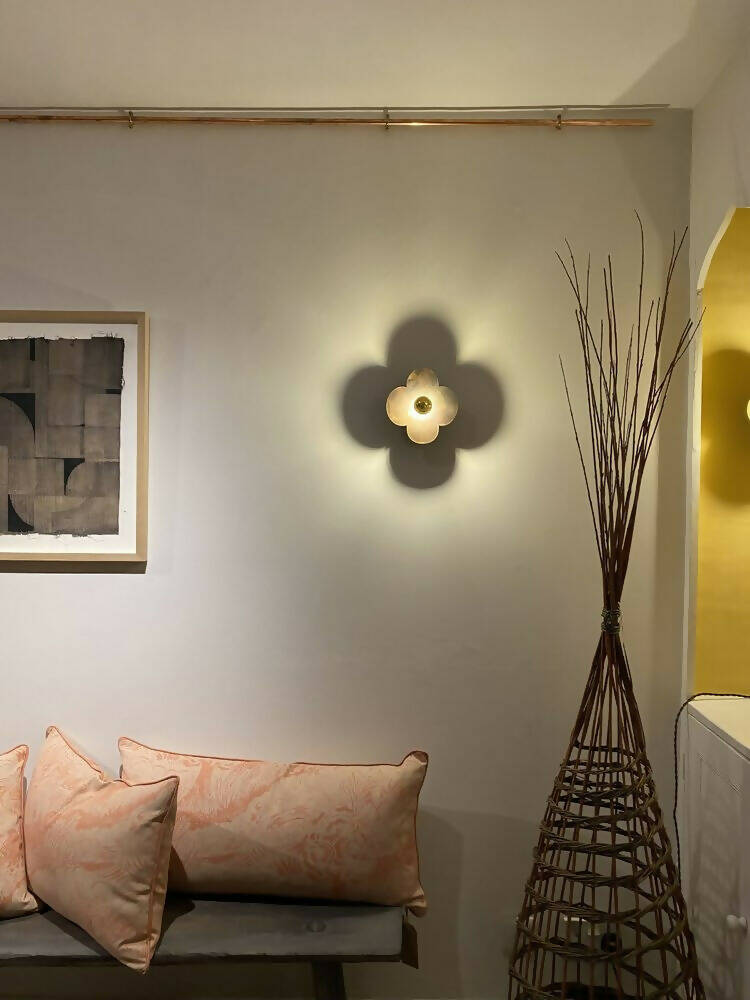 A wall light fixture with a gold-colored top and clear, possibly glass or acrylic, quatrefoil-shaped base,  available  to buy on the-salon.com. SALON curates the finest , unique, handmade pieces from the interior industry's best makers and brands. Shop luxury furniture, lighting, rugs, art, antiques and vintage pieces and accessories from SALON interior designed rooms.