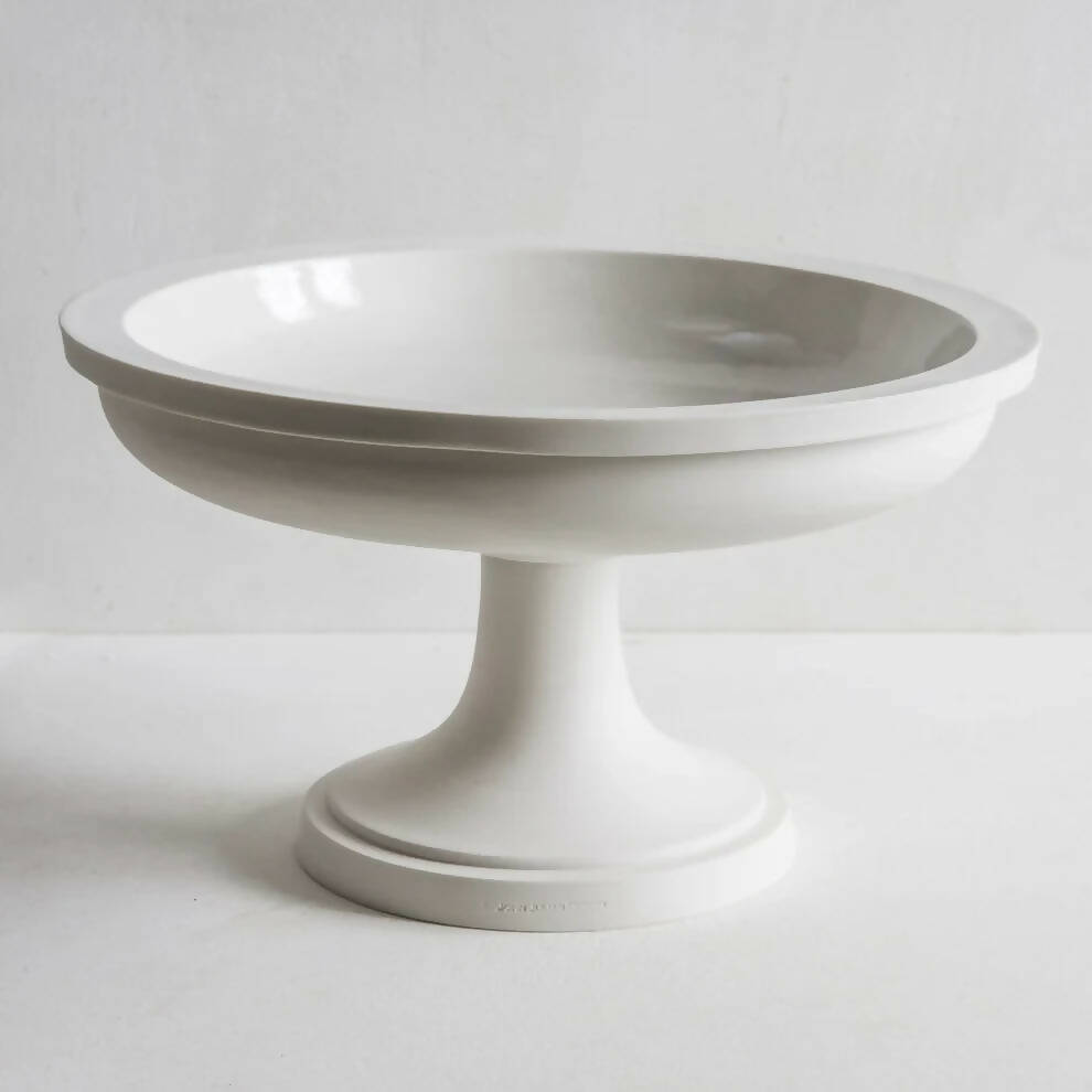 A white porcelain fruit stand with a sculptural foot, with a smooth, glazed finish on a white background,  available  to buy on the-salon.com. SALON curates the finest , unique, handmade pieces from the interior industry's best makers and brands. Shop luxury furniture, lighting, rugs, art, antiques and vintage pieces and accessories from SALON interior designed rooms.