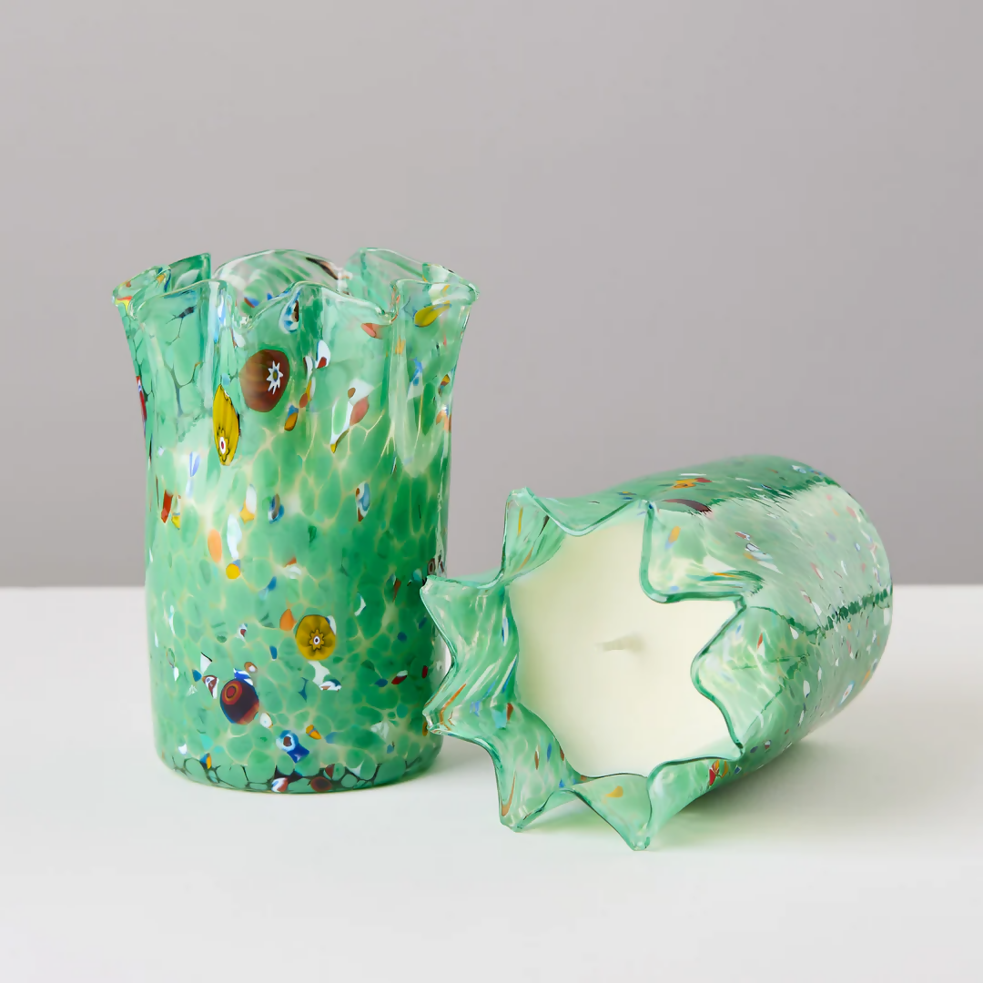 A custom hand-blown green glass candle holder with embedded colorful glass pieces, displayed alongside its lid, on a white surface,  available  to buy on the-salon.com. SALON curates the finest , unique, handmade pieces from the interior industry's best makers and brands. Shop luxury furniture, lighting, rugs, art, antiques and vintage pieces and accessories from SALON interior designed rooms.