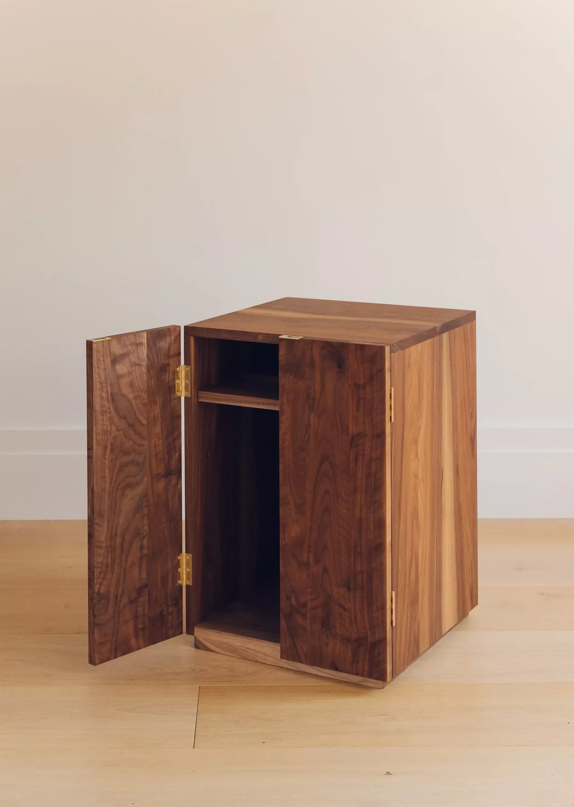 A wooden bedside cabinet with twin doors and a shelf, finished with brass butt hinges and finger plates, shown open to display the interior,  available  to buy on the-salon.com. SALON curates the finest , unique, handmade pieces from the interior industry's best makers and brands. Shop luxury furniture, lighting, rugs, art, antiques and vintage pieces and accessories from SALON interior designed rooms.