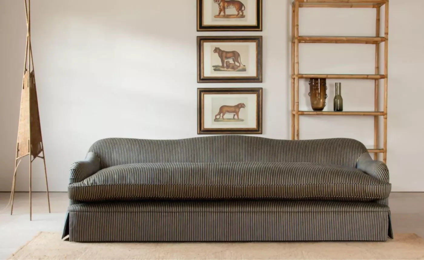 Gray sofa in a room with framed pictures on the wall and a wooden shelf.