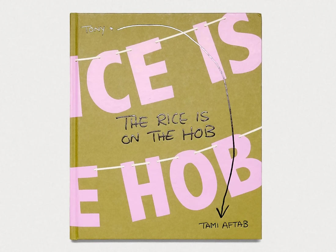 The image shows the cover of the book titled 'THE RICE IS ON THE HOB' with large pink letters on a beige background, and the author's name 'TAMI AFTAB' at the bottom,  available  to buy on the-salon.com. SALON curates the finest , unique, handmade pieces from the interior industry's best makers and brands. Shop luxury furniture, lighting, rugs, art, antiques and vintage pieces and accessories from SALON interior designed rooms.
