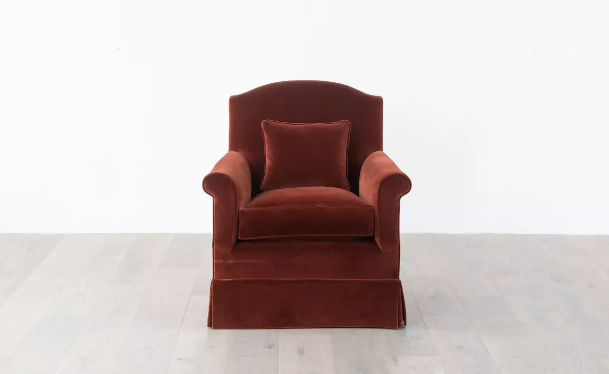 An elegant red upholstered armchair with a plush backrest and seat cushion, positioned in front of a white background,  available  to buy on the-salon.com. SALON curates the finest , unique, handmade pieces from the interior industry's best makers and brands. Shop luxury furniture, lighting, rugs, art, antiques and vintage pieces and accessories from SALON interior designed rooms.