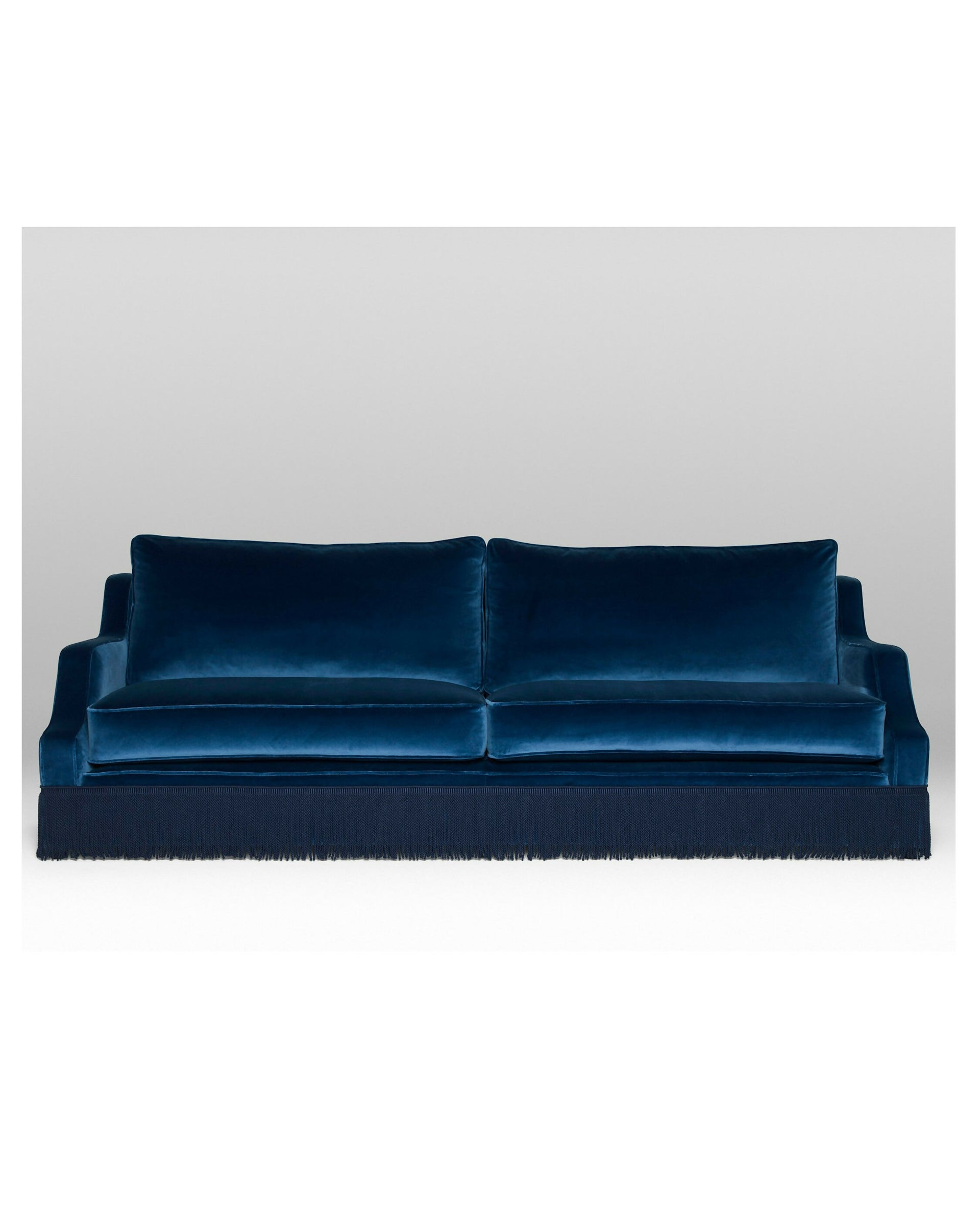A blue velvet sofa with plush seats and a tasseled fringe, named 'Large Atlanta Sofa by Orior', available  to buy on the-salon.com. SALON curates the finest , unique, handmade pieces from the interior industry's best makers and brands. Shop luxury furniture, lighting, rugs, art, antiques and vintage pieces and accessories from SALON interior designed rooms.