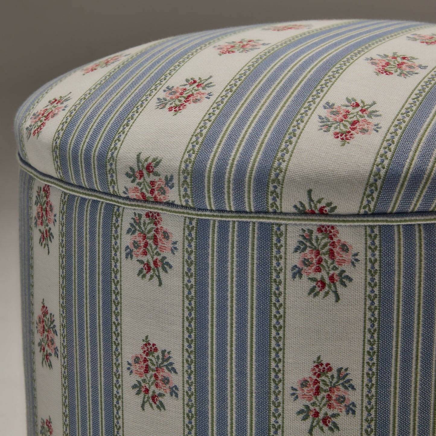 A close up of the  round footstool upholstered in a multicoloured fabric with stripes and floral patterns, featuring a silky champagne fringe at the bottom,  available  to buy on the-salon.com. SALON curates the finest , unique, handmade pieces from the interior industry's best makers and brands. Shop luxury furniture, lighting, rugs, art, antiques and vintage pieces and accessories from SALON interior designed rooms.