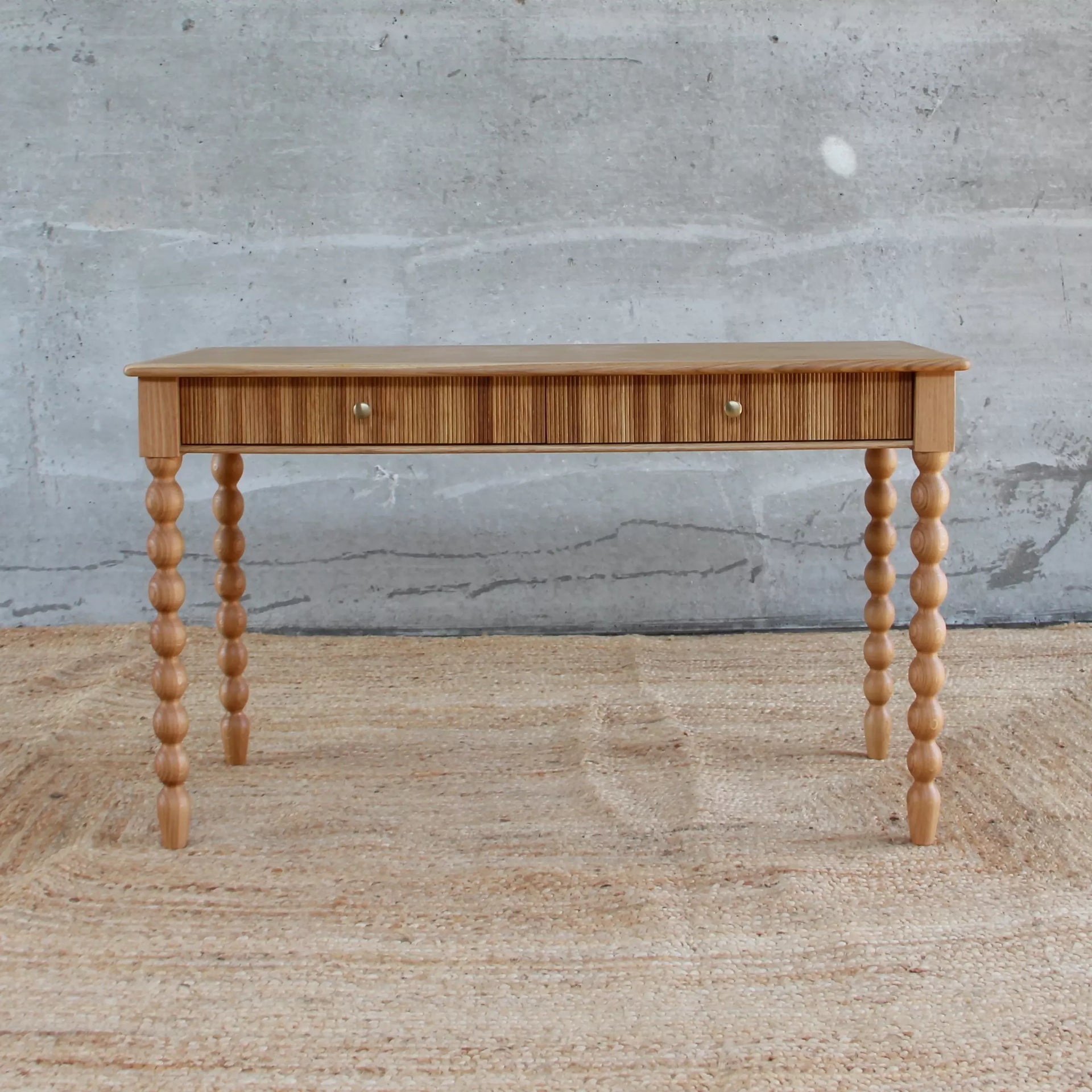 Wooden console table with spindle legs against a concrete wall,available to buy from the-salon.com. SALON curates the finest unique handmade pieces from the interior industry's best makers and brands. Shop luxury furniture, lighting, rugs, art, antiques and vintage pieces and accessories from SALON interior designed rooms. 