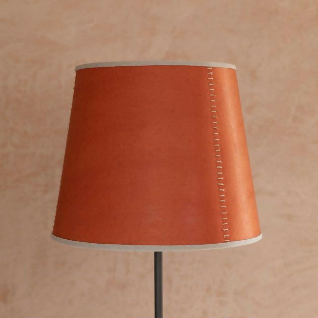 A tapered lampshade with a hand-stitched design, in Pompeian Buff colour, displayed on a stand against a neutral background, available  to buy on the-salon.com. SALON curates the finest , unique, handmade pieces from the interior industry's best makers and brands. Shop luxury furniture, lighting, rugs, art, antiques and vintage pieces and accessories from SALON interior designed rooms.