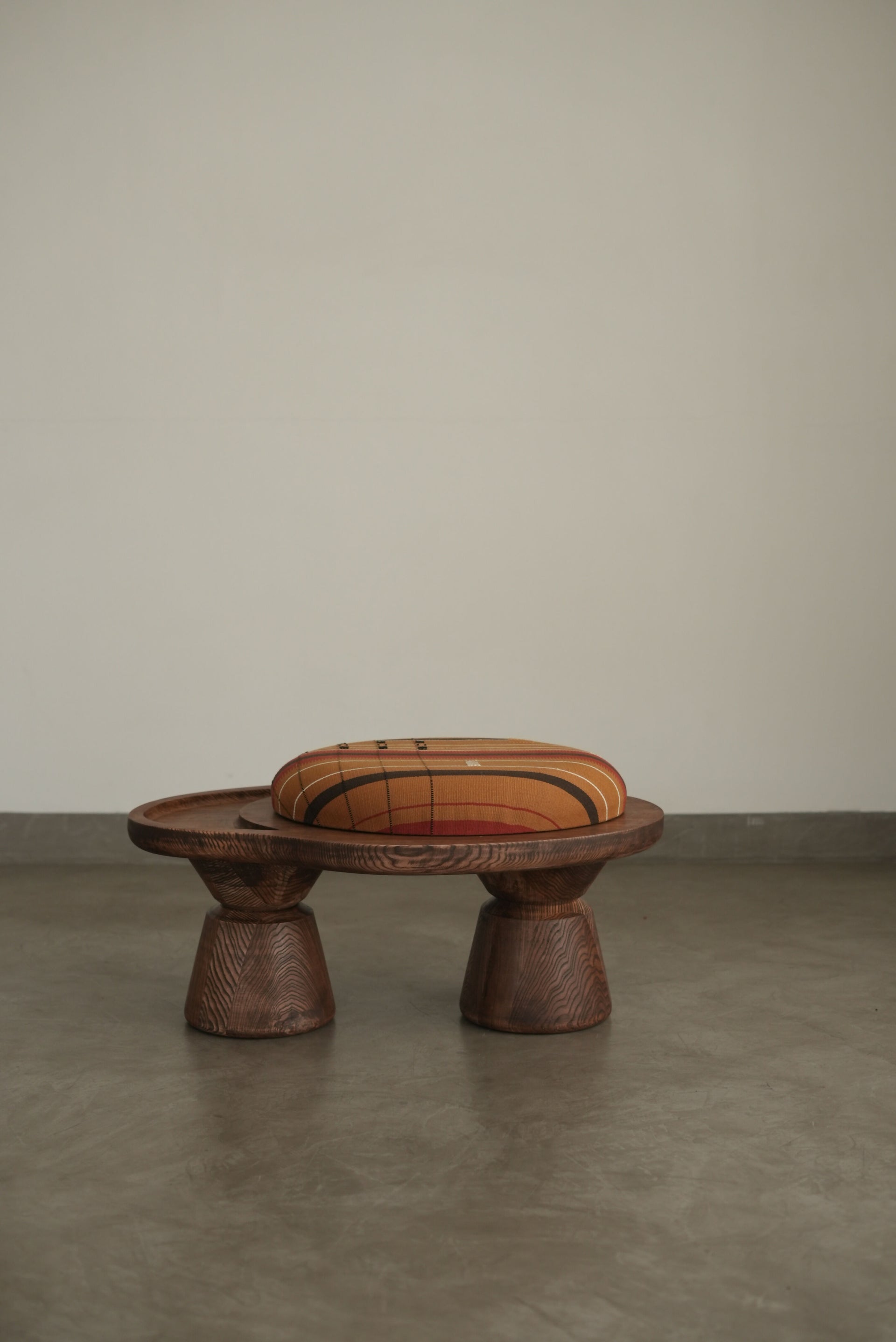 A sculptural single-seater ottoman with a curved body, upholstered in mustard color, on a concrete floor,  available  to buy on the-salon.com. SALON curates the finest , unique, handmade pieces from the interior industry's best makers and brands. Shop luxury furniture, lighting, rugs, art, antiques and vintage pieces and accessories from SALON interior designed rooms.