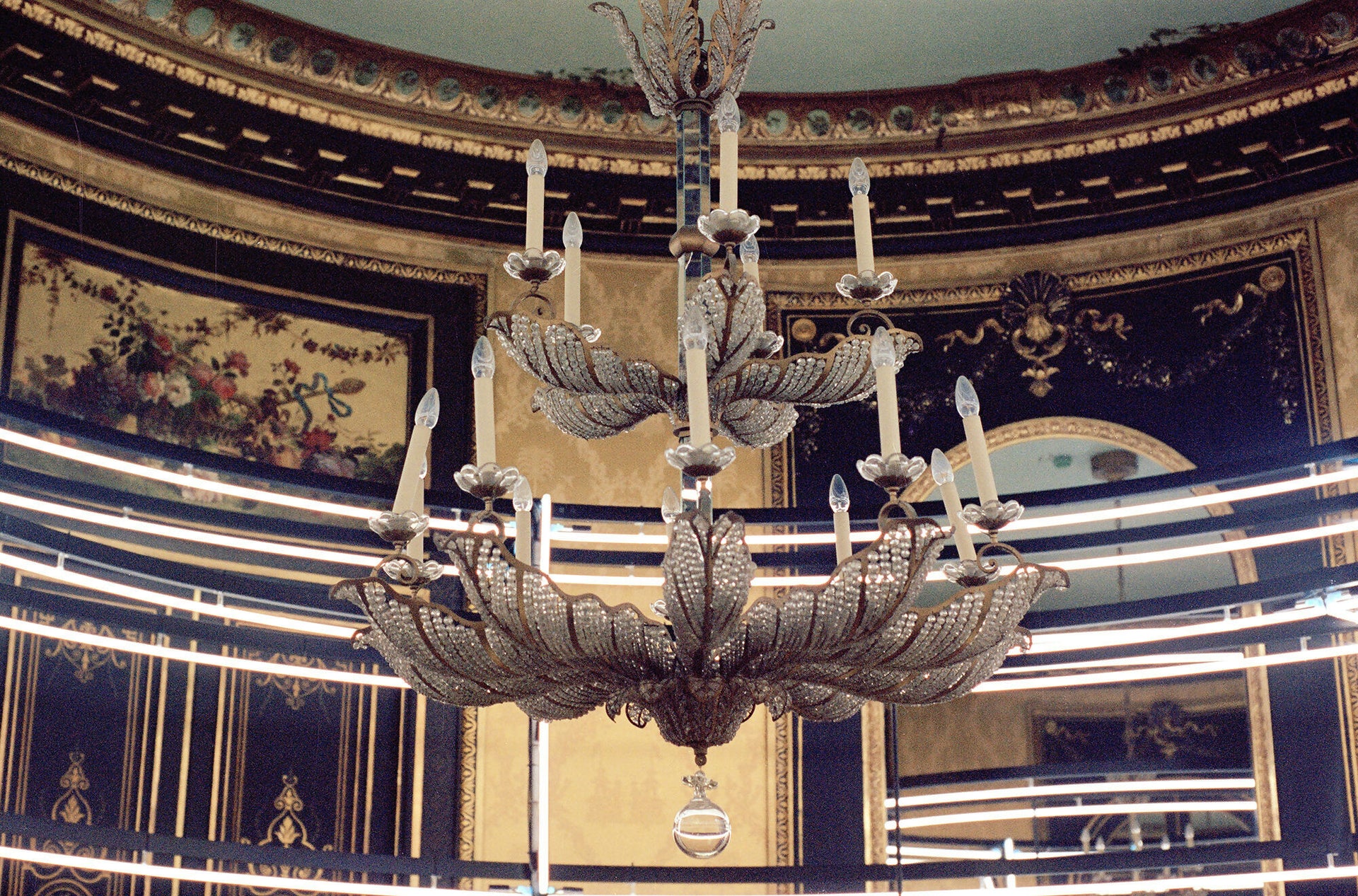 A photograph of chandelier shown in a classical ornate building with luminous lighting around it. 