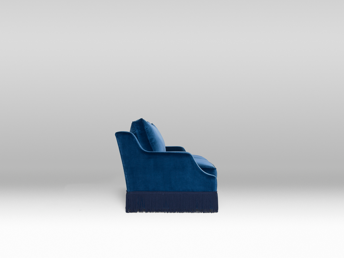 A blue velvet sofa with plush seats and a tasseled fringe, named 'Large Atlanta Sofa by Orior', available  to buy on the-salon.com. SALON curates the finest , unique, handmade pieces from the interior industry's best makers and brands. Shop luxury furniture, lighting, rugs, art, antiques and vintage pieces and accessories from SALON interior designed rooms.