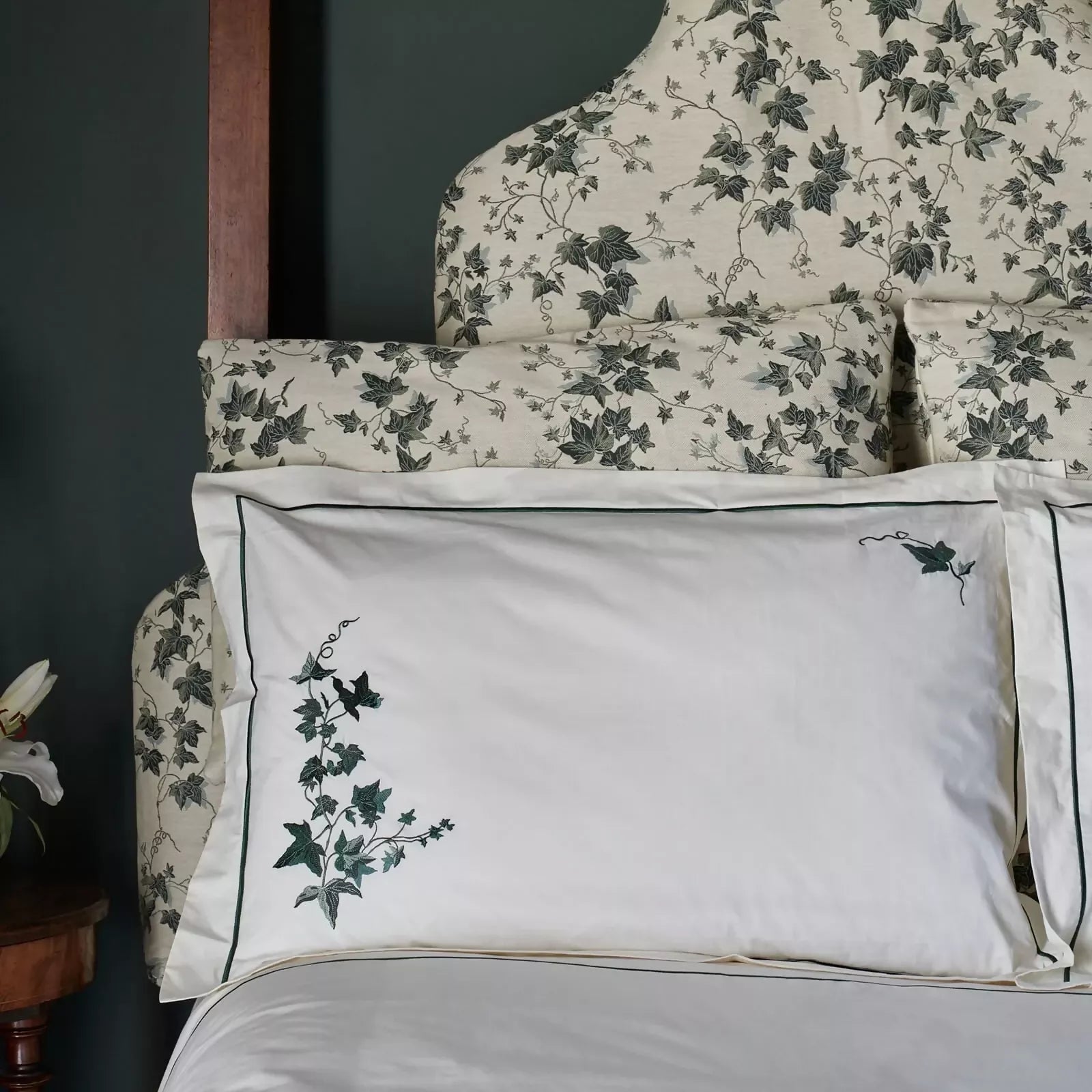 Floral headboard and white pillows with green embroidery on a dark wall.