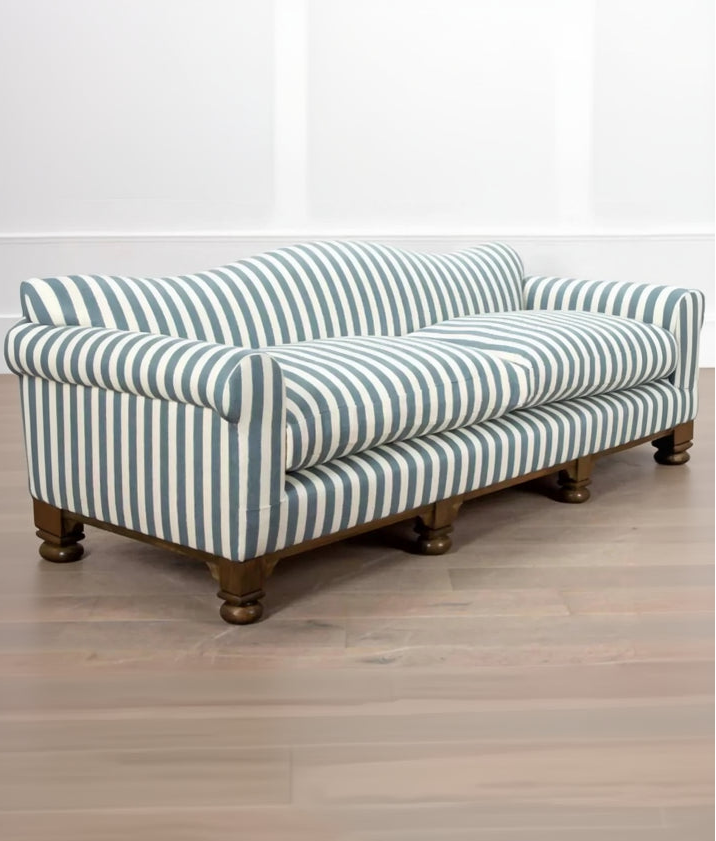 A blue and white striped camel back sofa with solid oak turned legs in a room with decorative items on top, available  to buy on the-salon.com. SALON curates the finest , unique, handmade pieces from the interior industry's best makers and brands. Shop luxury furniture, lighting, rugs, art, antiques and vintage pieces and accessories from SALON interior designed rooms.