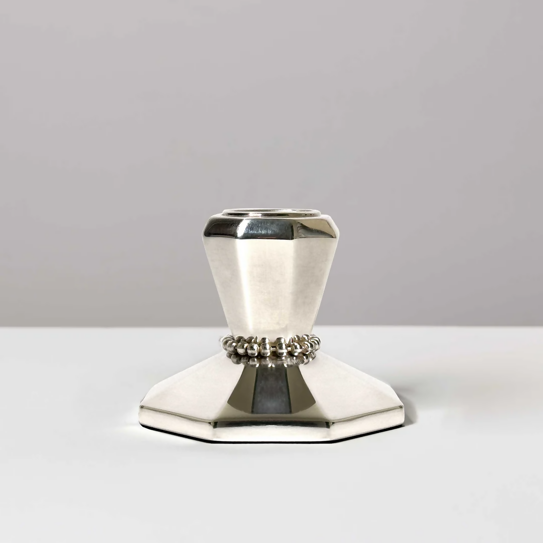 A silver candle stick on a white background, featuring intricate beaded detailing around the neck and an angular base,  available  to buy on the-salon.com. SALON curates the finest , unique, handmade pieces from the interior industry's best makers and brands. Shop luxury furniture, lighting, rugs, art, antiques and vintage pieces and accessories from SALON interior designed rooms.