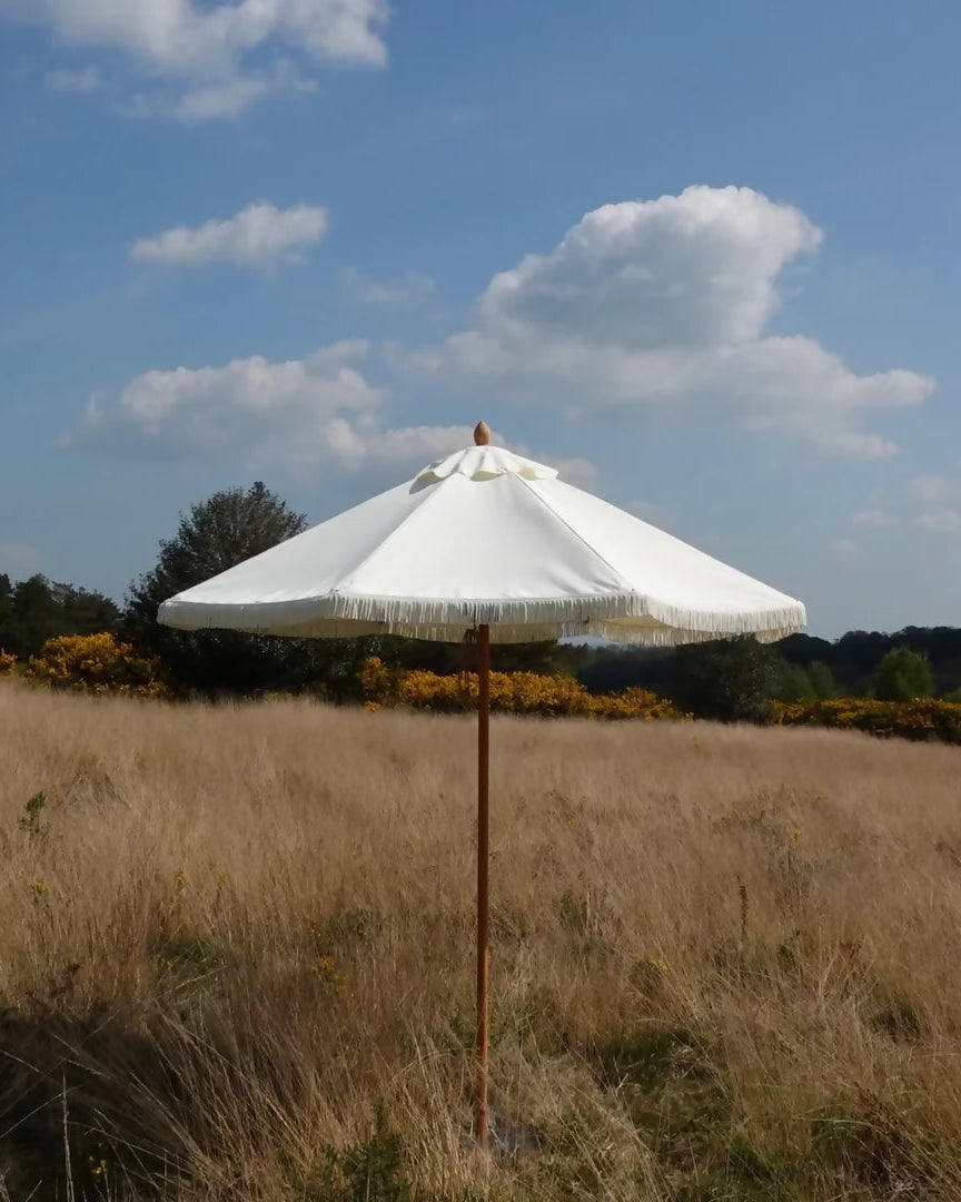 White umbrella with a wooden stand in a field under a blue sky with clouds