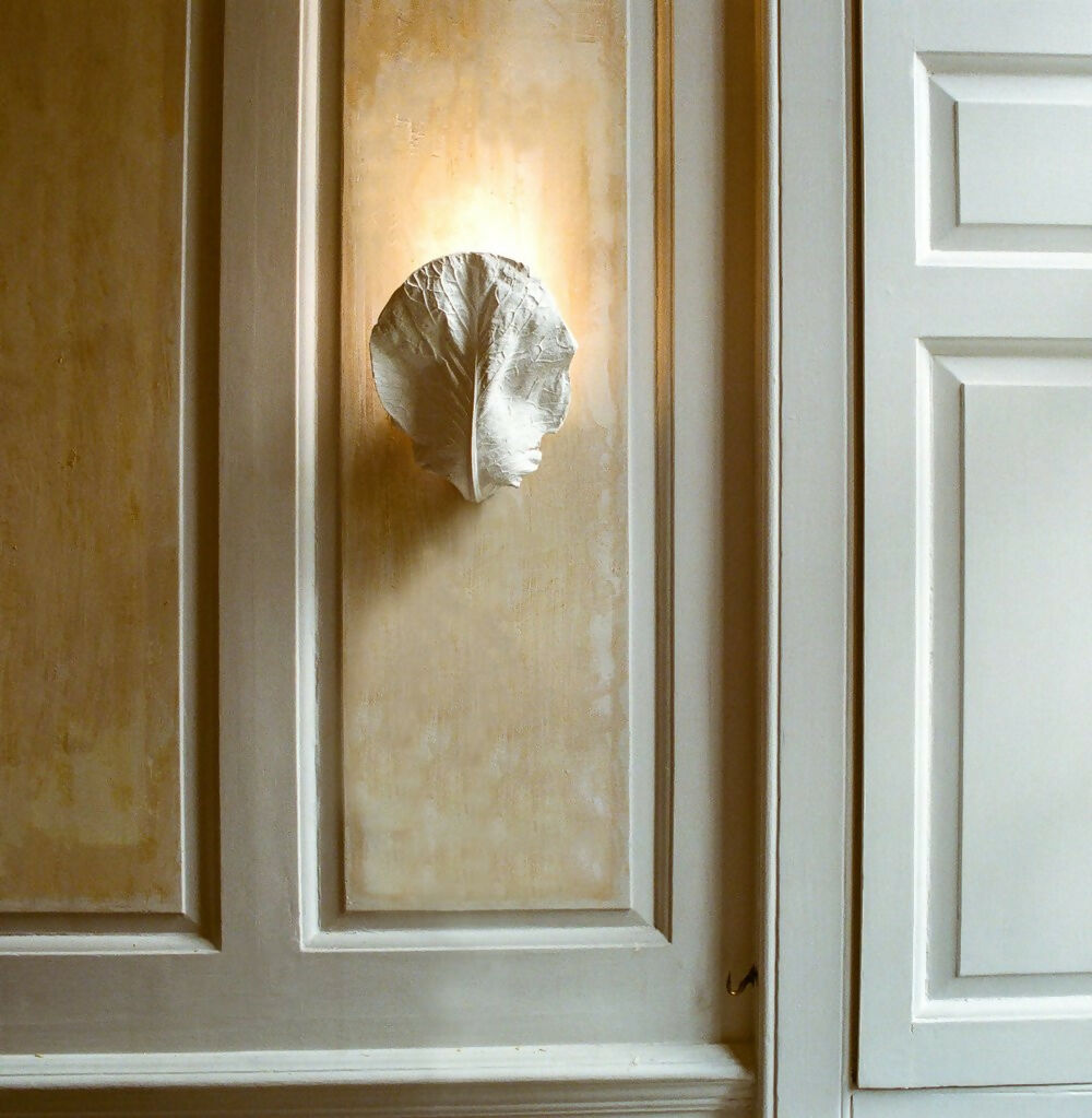 A plaster wall light fixture in the shape of a hispi cabbage leaf, displayed against a neutral background,  available  to buy on the-salon.com. SALON curates the finest , unique, handmade pieces from the interior industry's best makers and brands. Shop luxury furniture, lighting, rugs, art, antiques and vintage pieces and accessories from SALON interior designed rooms.