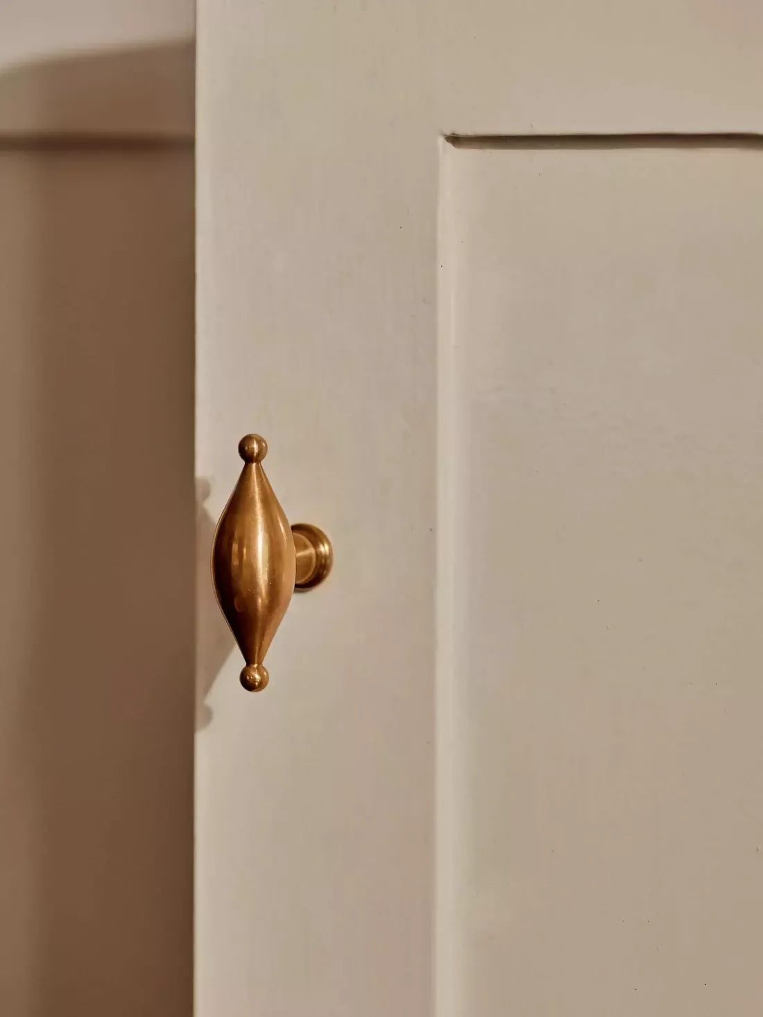 A gold-colored metal pull handle in an elliptical shape mounted on a white door, available  to buy on the-salon.com. SALON curates the finest , unique, handmade pieces from the interior industry's best makers and brands. Shop luxury furniture, lighting, rugs, art, antiques and vintage pieces and accessories from SALON interior designed rooms.