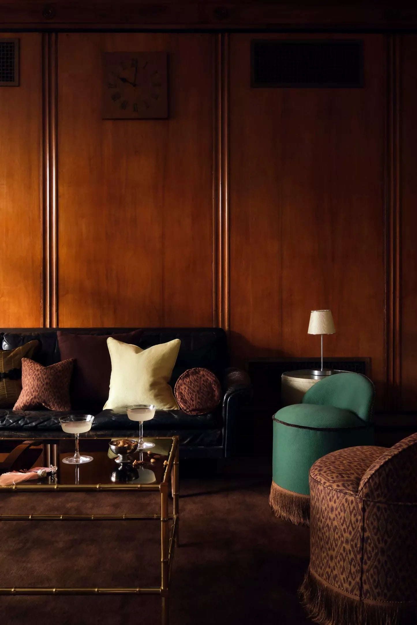 Brown cylindrical pillow with a leopard print pattern on a beige background, displayed in a room with hardwood walls and two ottomans and a glass coffee table,   available  to buy on the-salon.com. SALON curates the finest , unique, handmade pieces from the interior industry's best makers and brands. Shop luxury furniture, lighting, rugs, art, antiques and vintage pieces and accessories from SALON interior designed rooms.