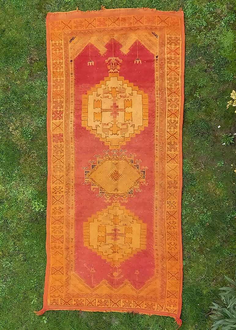 A vintage wool hand knotted rug with an open field design featuring geometric patterns in orange, red, and yellow shades, available  to buy on the-salon.com. SALON curates the finest , unique, handmade pieces from the interior industry's best makers and brands. Shop luxury furniture, lighting, rugs, art, antiques and vintage pieces and accessories from SALON interior designed rooms.