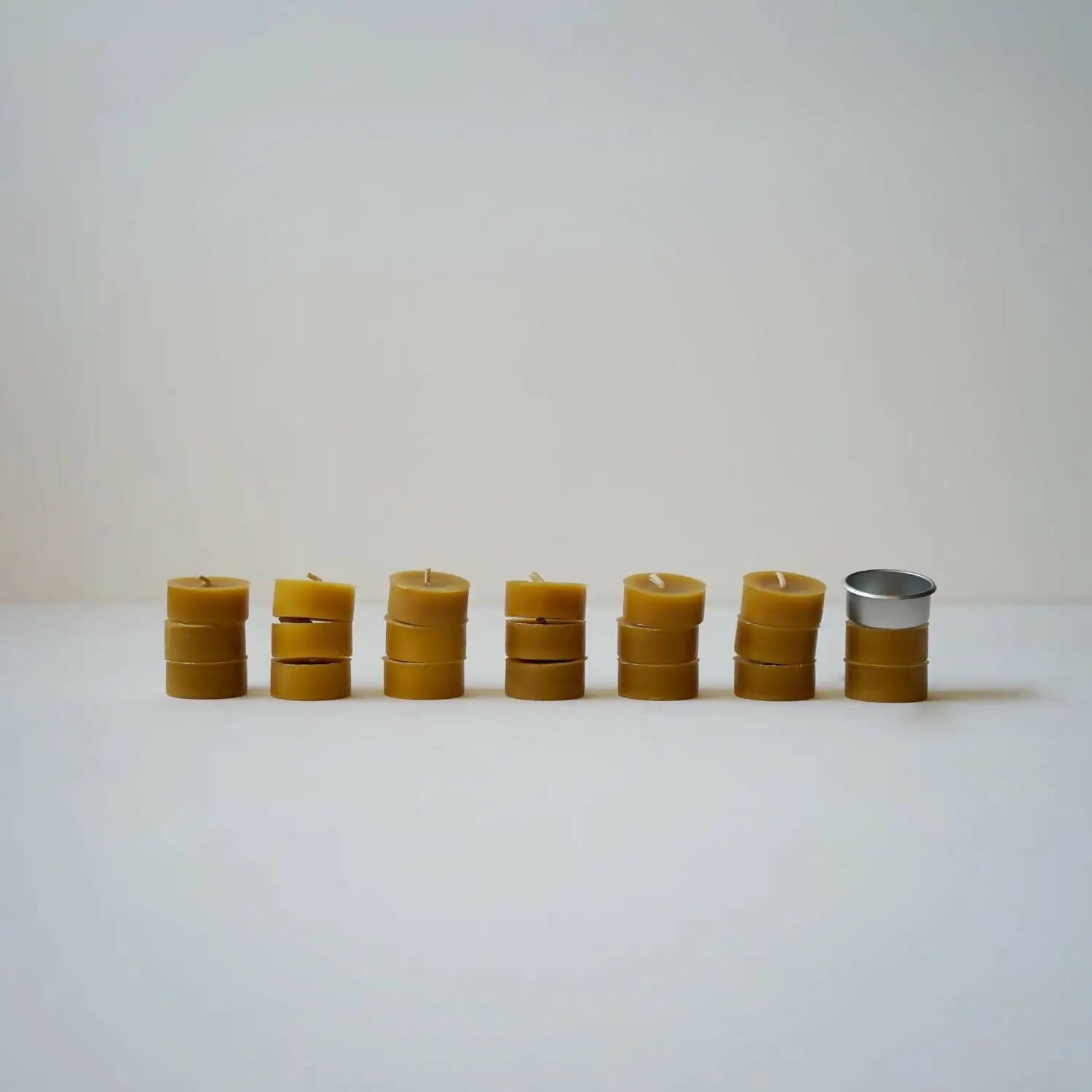 A row of organic beeswax tealights arranged on a white surface with a tealight holder to the side, available  to buy on the-salon.com. SALON curates the finest , unique, handmade pieces from the interior industry's best makers and brands. Shop luxury furniture, lighting, rugs, art, antiques and vintage pieces and accessories from SALON interior designed rooms.