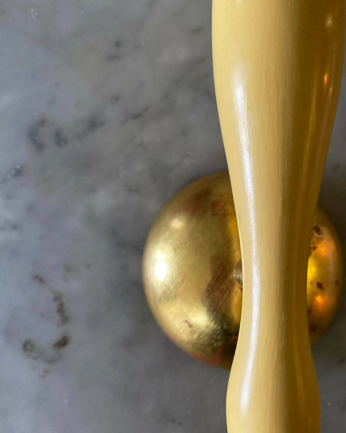 A close up on the wall light fixture with a yellow, stem-like structure and a white conical shade, mounted on a gold-colored plate, available  to buy on the-salon.com. SALON curates the finest , unique, handmade pieces from the interior industry's best makers and brands. Shop luxury furniture, lighting, rugs, art, antiques and vintage pieces and accessories from SALON interior designed rooms.