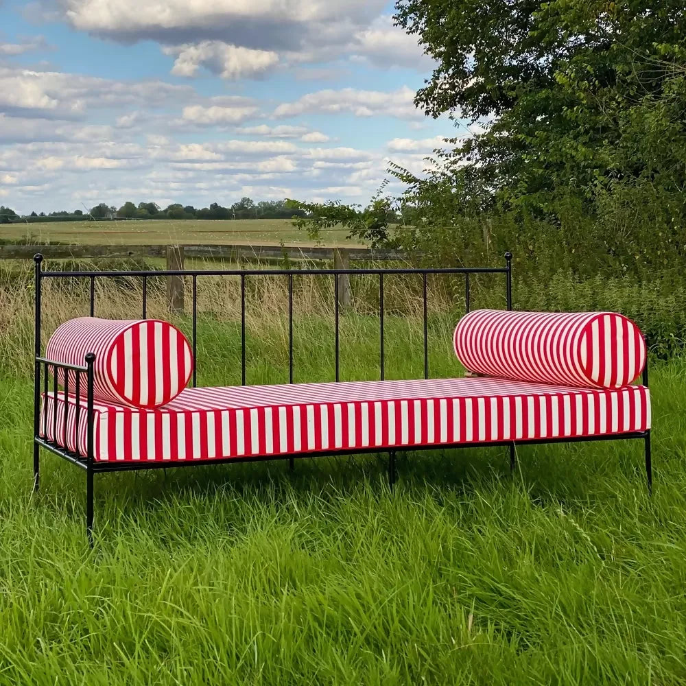 Red and white striped bench in a grassy field with a blue sky and trees in the background