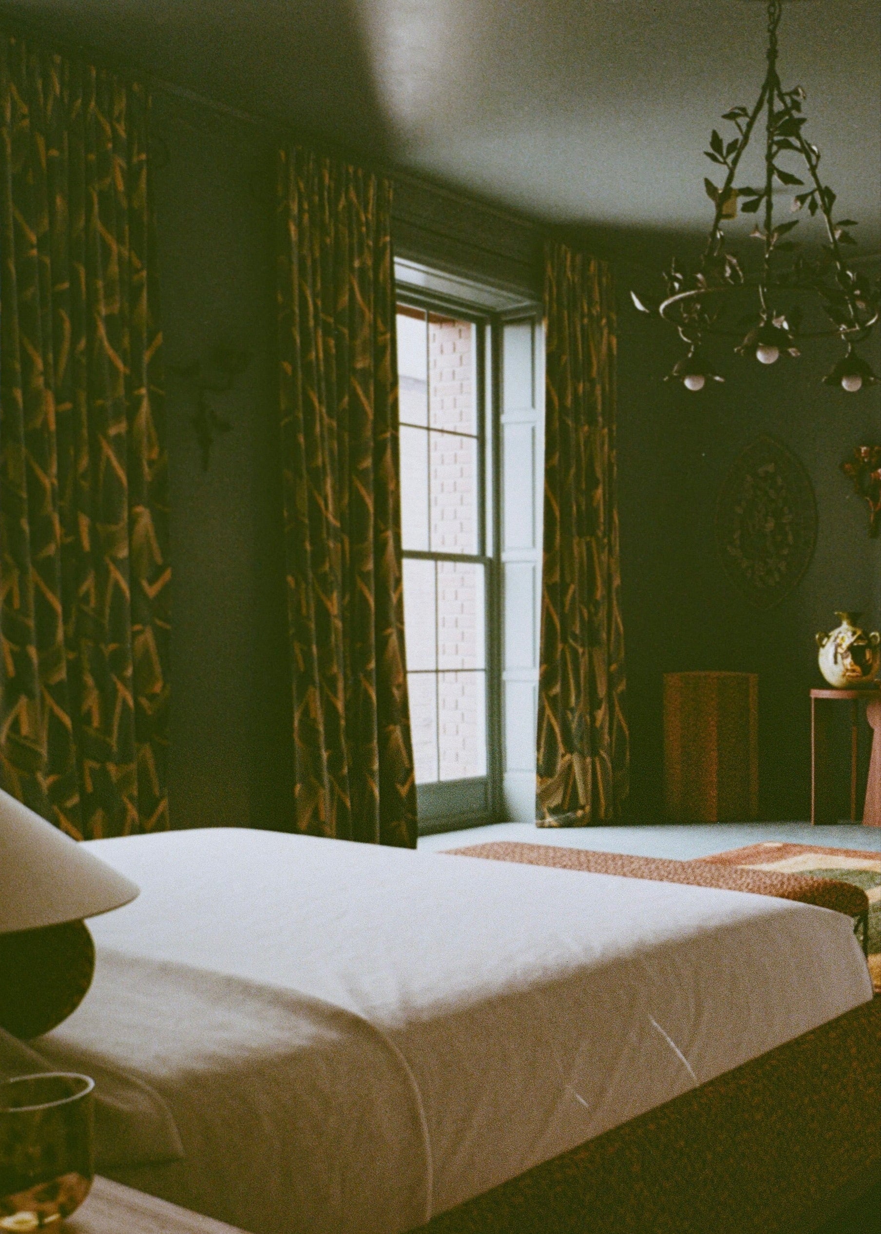 Room with patterned curtains, a bed, and a chandelier.