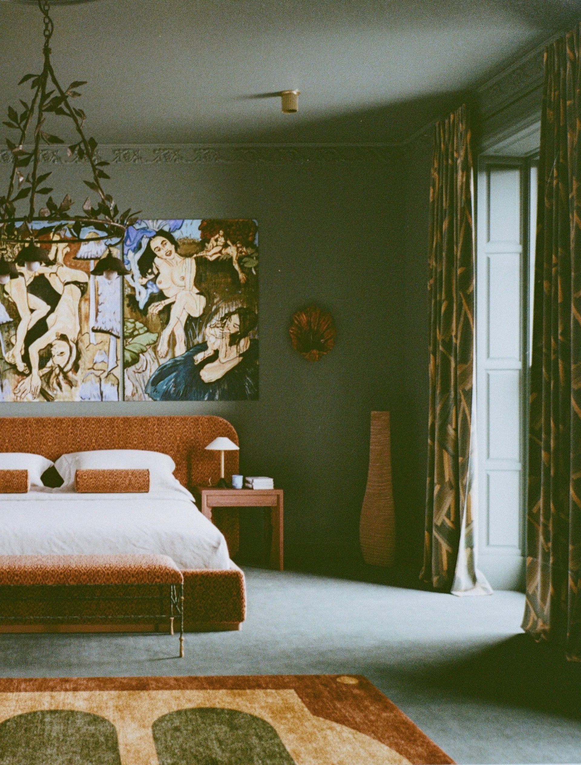 Decorative interior of a room with a large painting on the wall, a bed with orange headboard, and a vase.
