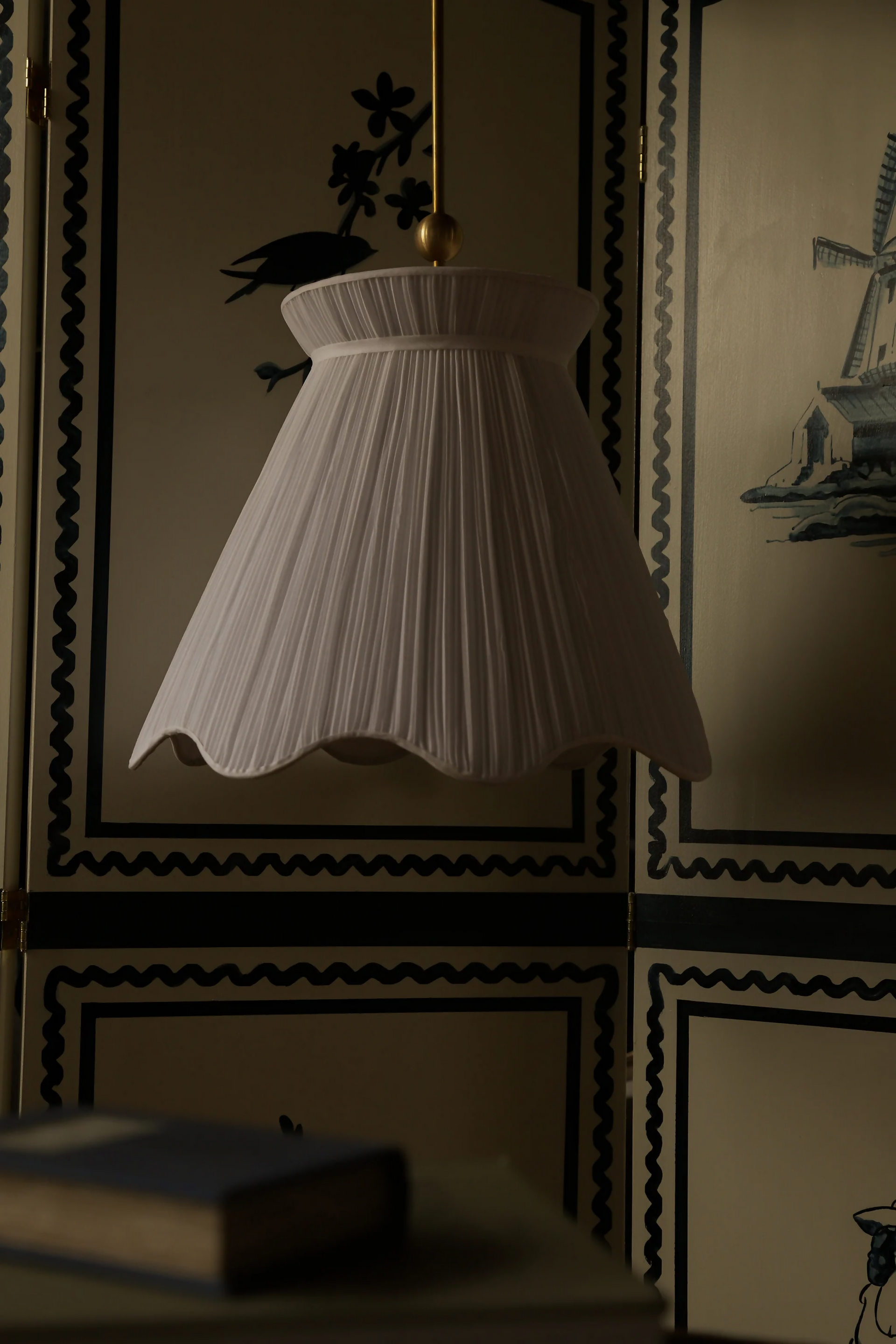 A white pleated pendant light hanging in a room with decorative walls, displaying a soft illumination, available  to buy on the-salon.com. SALON curates the finest , unique, handmade pieces from the interior industry's best makers and brands. Shop luxury furniture, lighting, rugs, art, antiques and vintage pieces and accessories from SALON interior designed rooms.