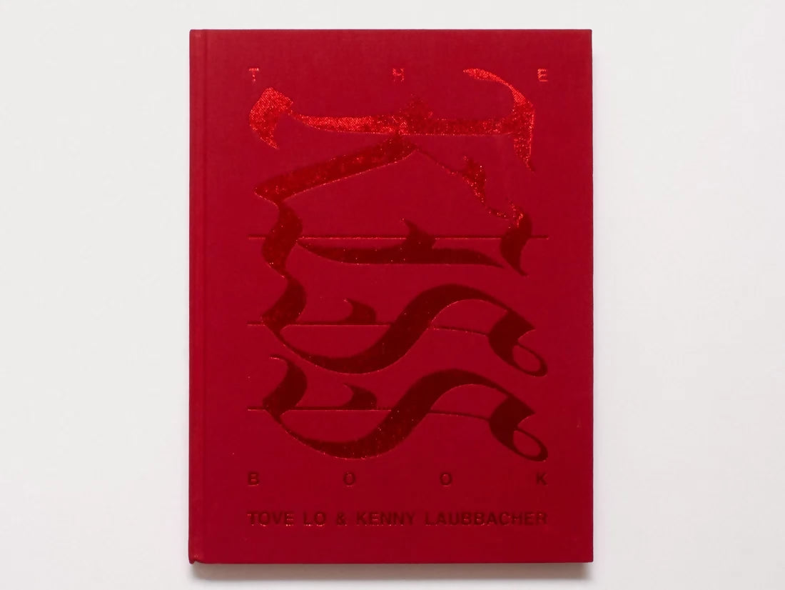 A red hardcover book titled 'THE BOOK' with a raised, embossed abstract design on the cover, photographed against a plain white background.
