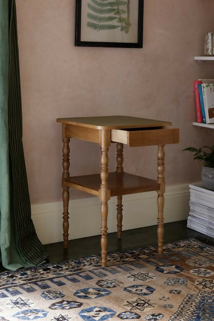 A brown wooden bedside table with a leather top, placed on a patterned carpet,  available  to buy on the-salon.com. SALON curates the finest , unique, handmade pieces from the interior industry's best makers and brands. Shop luxury furniture, lighting, rugs, art, antiques and vintage pieces and accessories from SALON interior designed rooms.