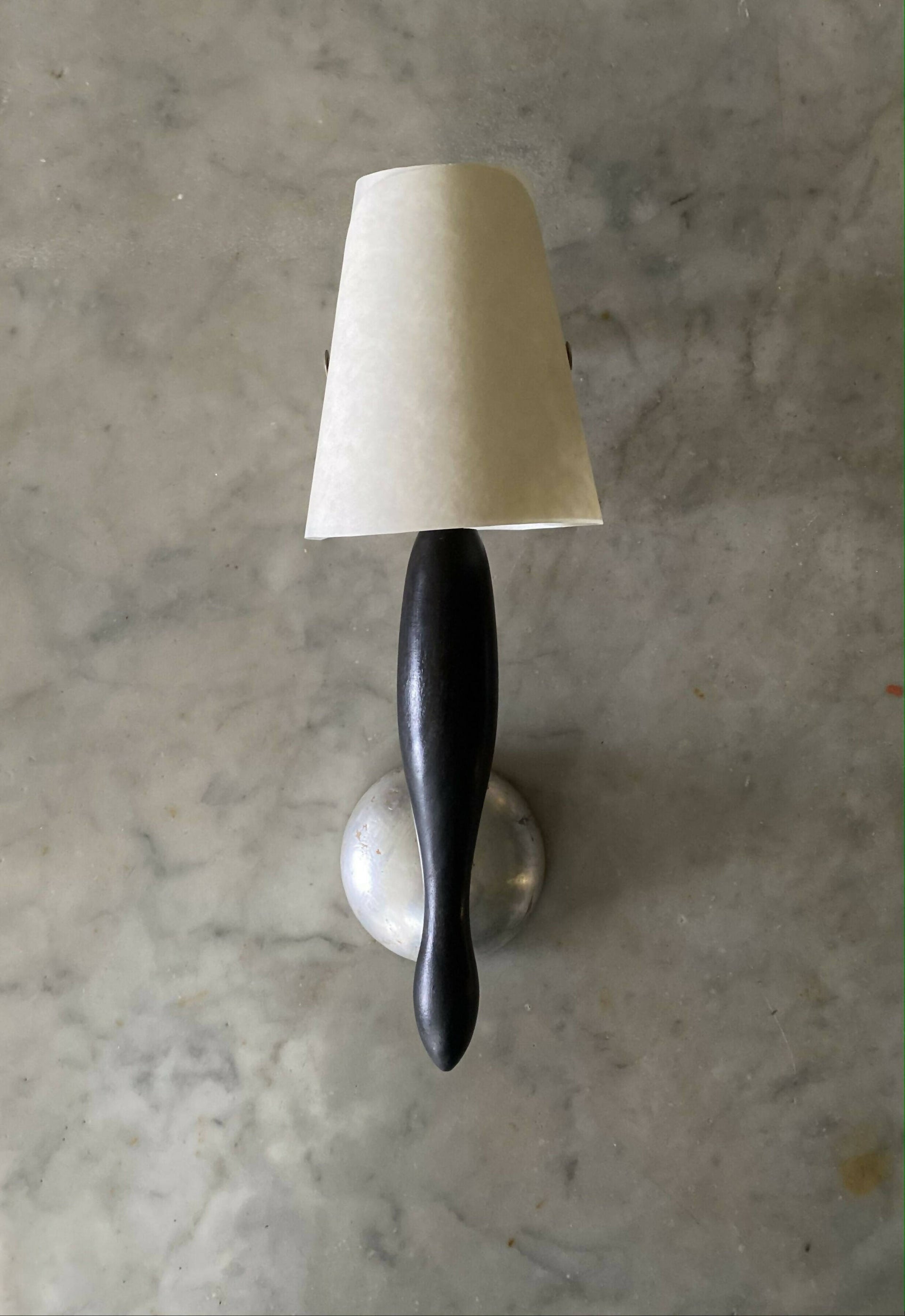 A wall light fixture with a black, stem-like structure and a white conical shade, mounted on a silver-colored plate, available  to buy on the-salon.com. SALON curates the finest , unique, handmade pieces from the interior industry's best makers and brands. Shop luxury furniture, lighting, rugs, art, antiques and vintage pieces and accessories from SALON interior designed rooms.