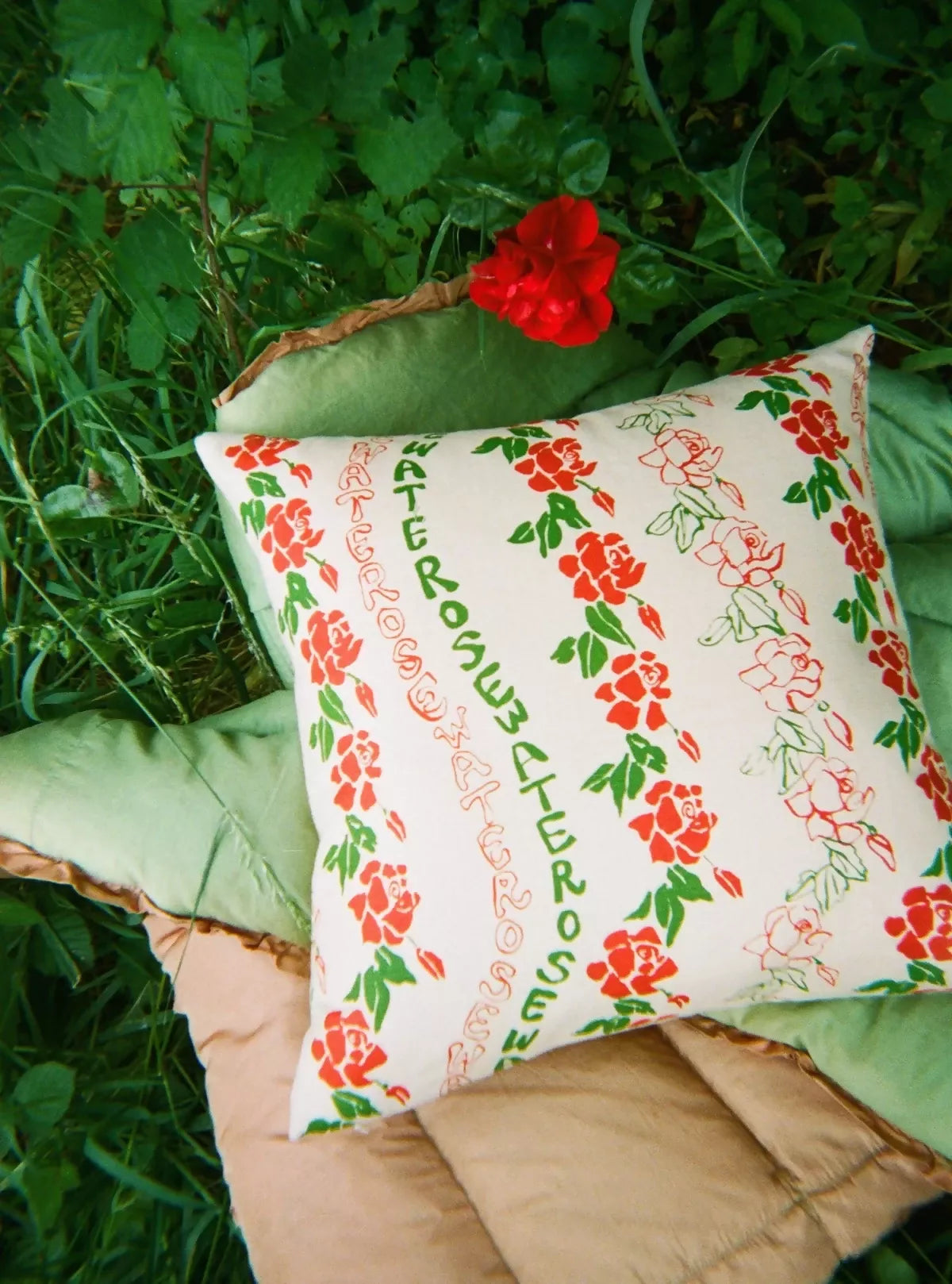 A rectangular cushion with a floral pattern, featuring red flowers and green leaves, resting on a bed of leaves,  available  to buy on the-salon.com. SALON curates the finest , unique, handmade pieces from the interior industry's best makers and brands. Shop luxury furniture, lighting, rugs, art, antiques and vintage pieces and accessories from SALON interior designed rooms.