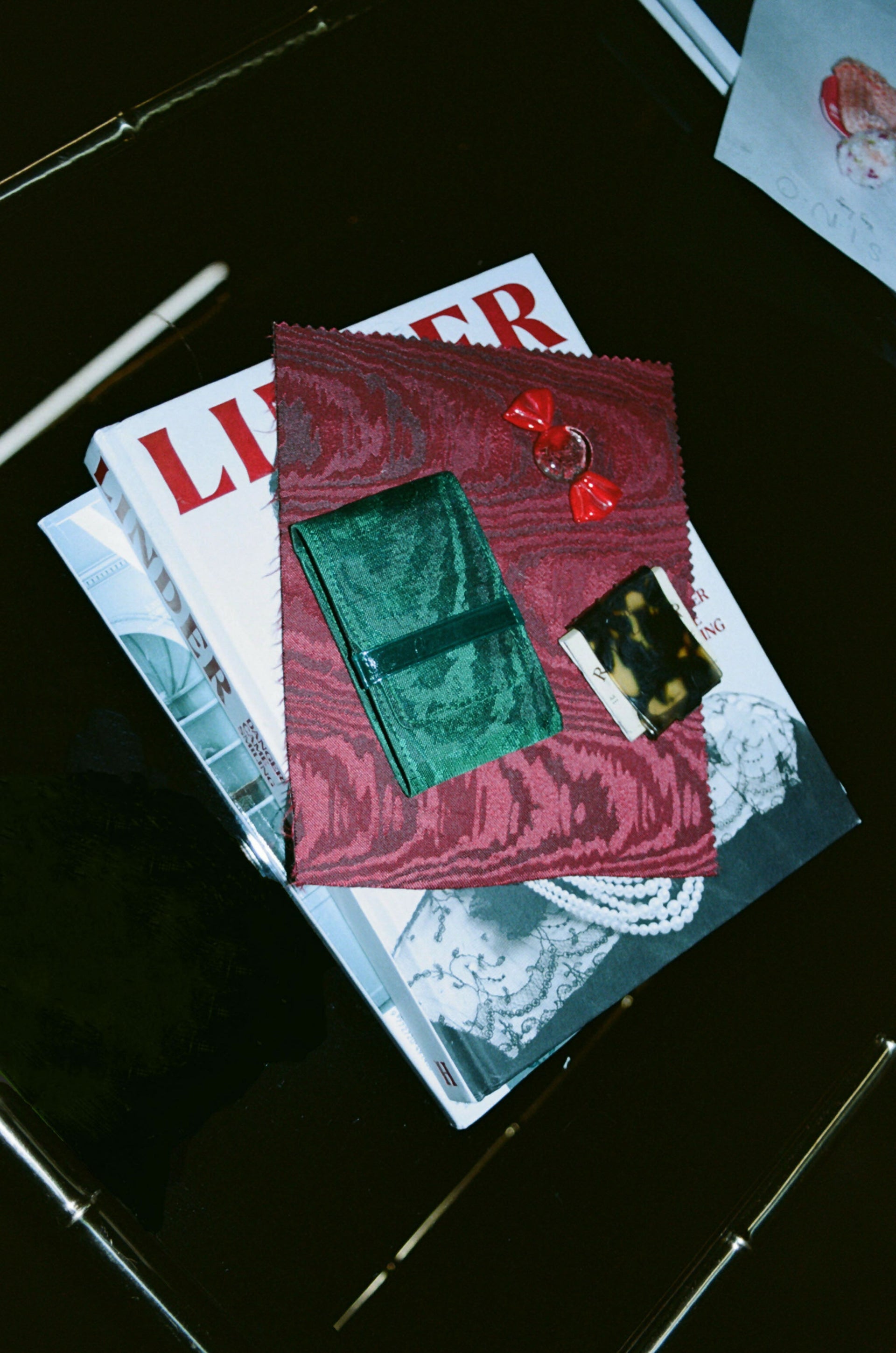 Red fabric pouch with a green interior on top of a magazine,  available  to buy on the-salon.com. SALON curates the finest , unique, handmade pieces from the interior industry's best makers and brands. Shop luxury furniture, lighting, rugs, art, antiques and vintage pieces and accessories from SALON interior designed rooms.