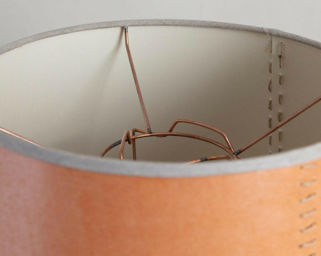 A tapered lampshade with a hand-stitched design, in Pompeian Buff colour, displayed on a stand against a neutral background, available  to buy on the-salon.com. SALON curates the finest , unique, handmade pieces from the interior industry's best makers and brands. Shop luxury furniture, lighting, rugs, art, antiques and vintage pieces and accessories from SALON interior designed rooms.