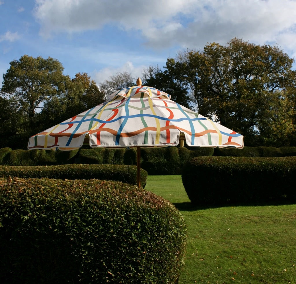 Colorful umbrella in a garden setting with trees and grass.