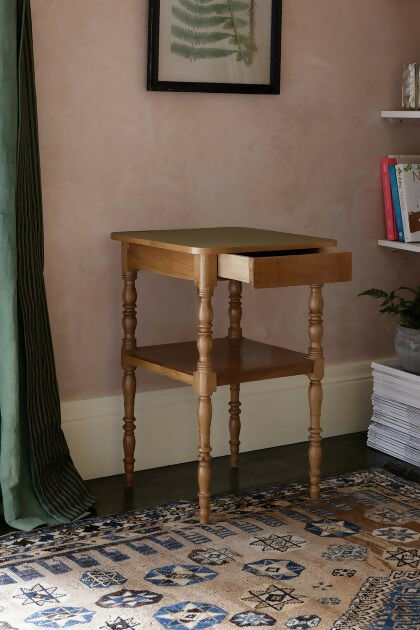A brown wooden bedside table with a leather top, placed on a patterned carpet,  available  to buy on the-salon.com. SALON curates the finest , unique, handmade pieces from the interior industry's best makers and brands. Shop luxury furniture, lighting, rugs, art, antiques and vintage pieces and accessories from SALON interior designed rooms.