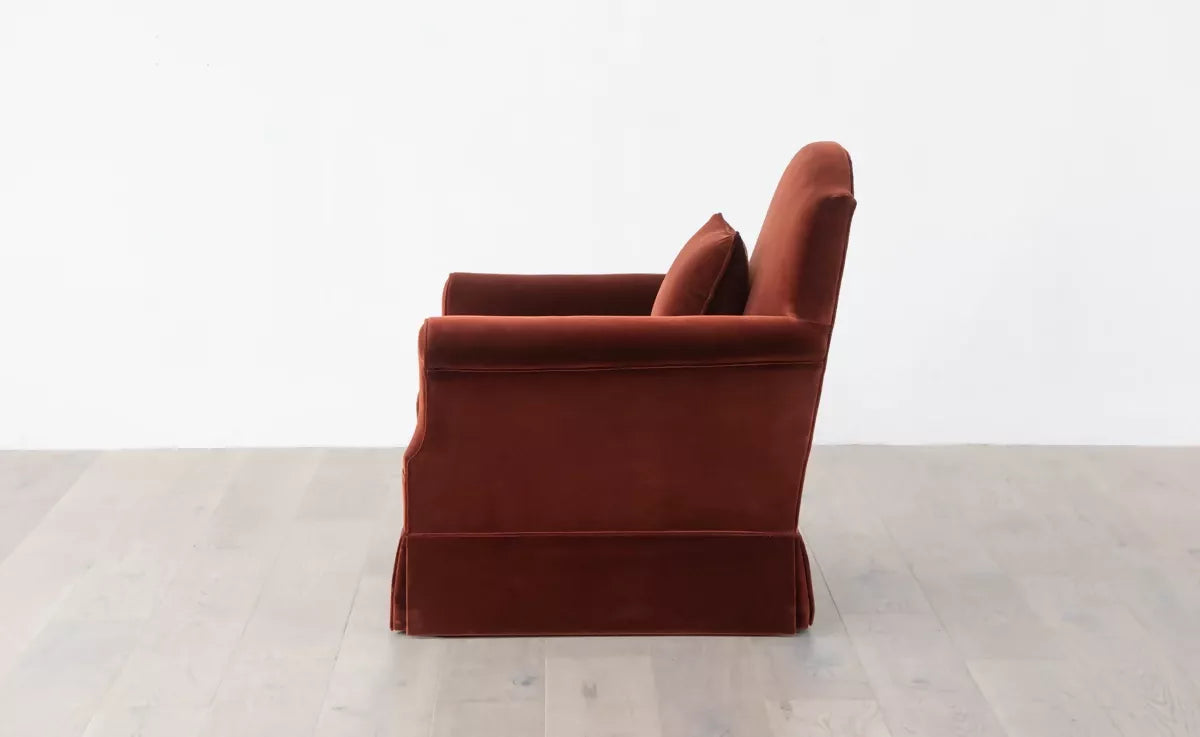 An elegant red upholstered armchair with a plush backrest and seat cushion, positioned in side angle in front of a white background,  available  to buy on the-salon.com. SALON curates the finest , unique, handmade pieces from the interior industry's best makers and brands. Shop luxury furniture, lighting, rugs, art, antiques and vintage pieces and accessories from SALON interior designed rooms.