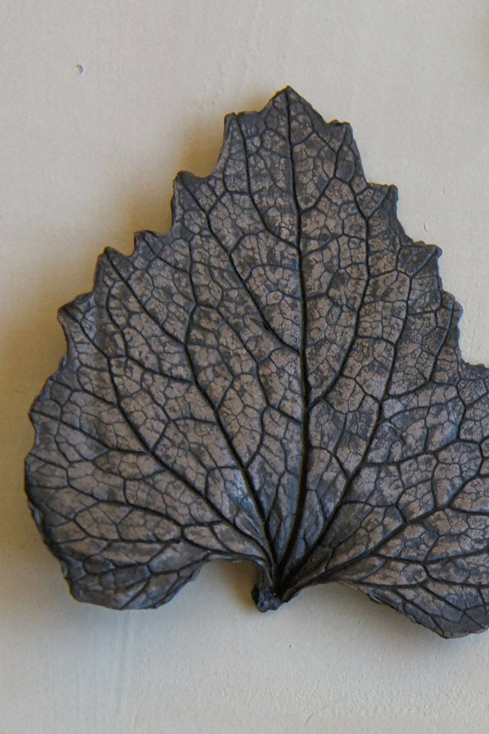 Close up of a bronze leaf-shaped sculpture on a light background, available  to buy on the-salon.com. SALON curates the finest , unique, handmade pieces from the interior industry's best makers and brands. Shop luxury furniture, lighting, rugs, art, antiques and vintage pieces and accessories from SALON interior designed rooms.