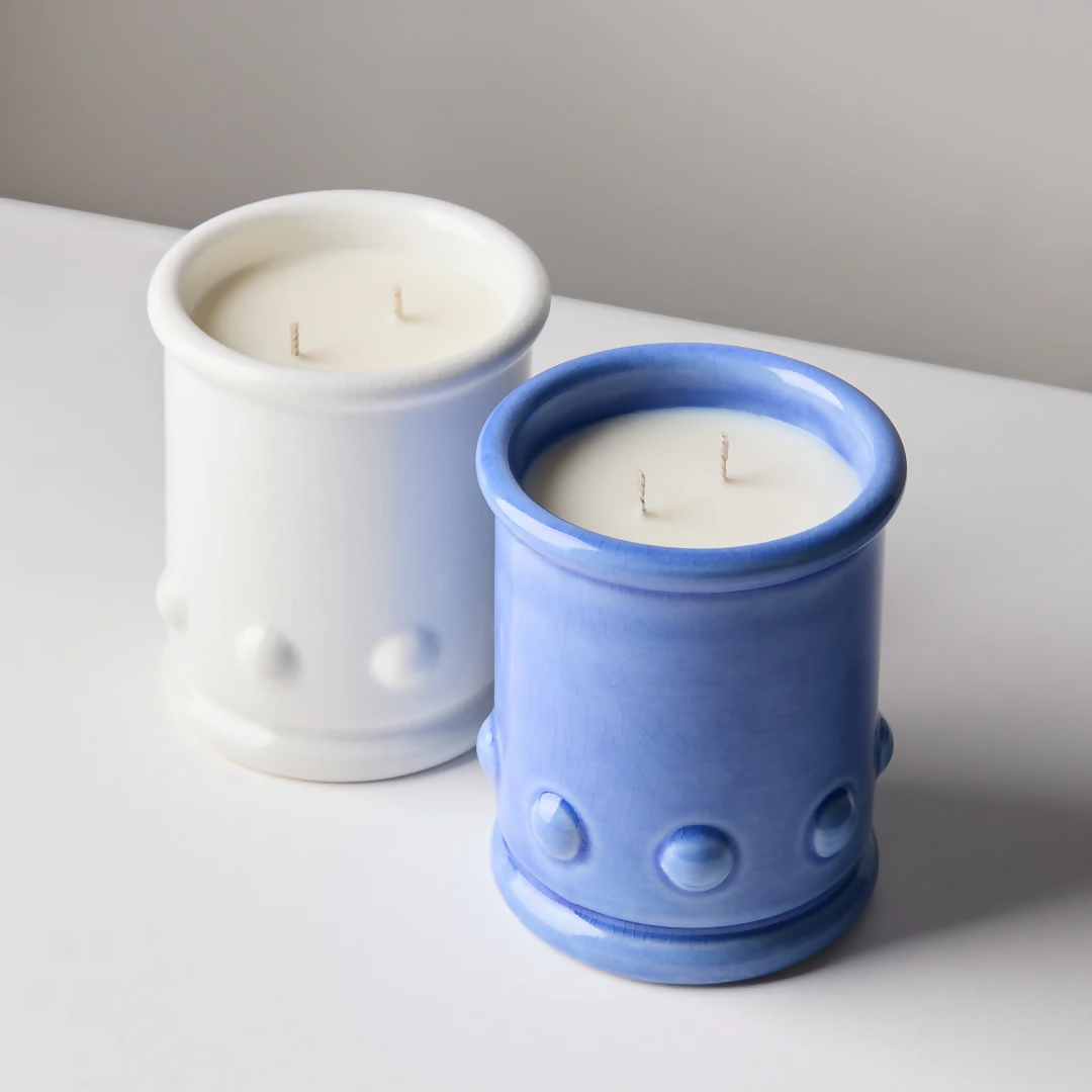 Blue and white ceramic candle vessels with spherical detailing on the sides, with a candle visible at the top. The vessel is placed against a neutral background,  available  to buy on the-salon.com. SALON curates the finest , unique, handmade pieces from the interior industry's best makers and brands. Shop luxury furniture, lighting, rugs, art, antiques and vintage pieces and accessories from SALON interior designed rooms.