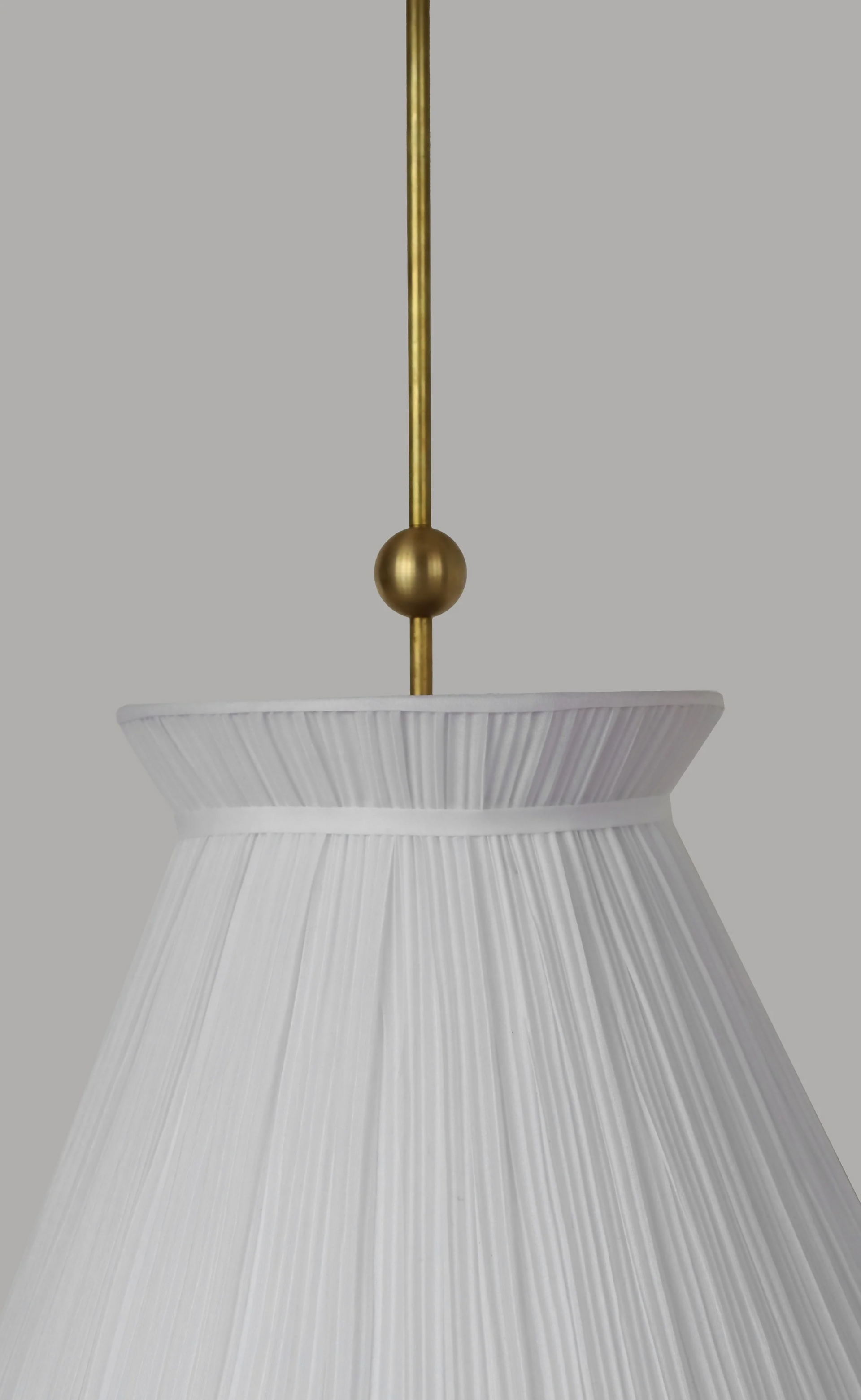 A white pleated pendant light hanging in a room with decorative walls, displaying a soft illumination, available  to buy on the-salon.com. SALON curates the finest , unique, handmade pieces from the interior industry's best makers and brands. Shop luxury furniture, lighting, rugs, art, antiques and vintage pieces and accessories from SALON interior designed rooms.