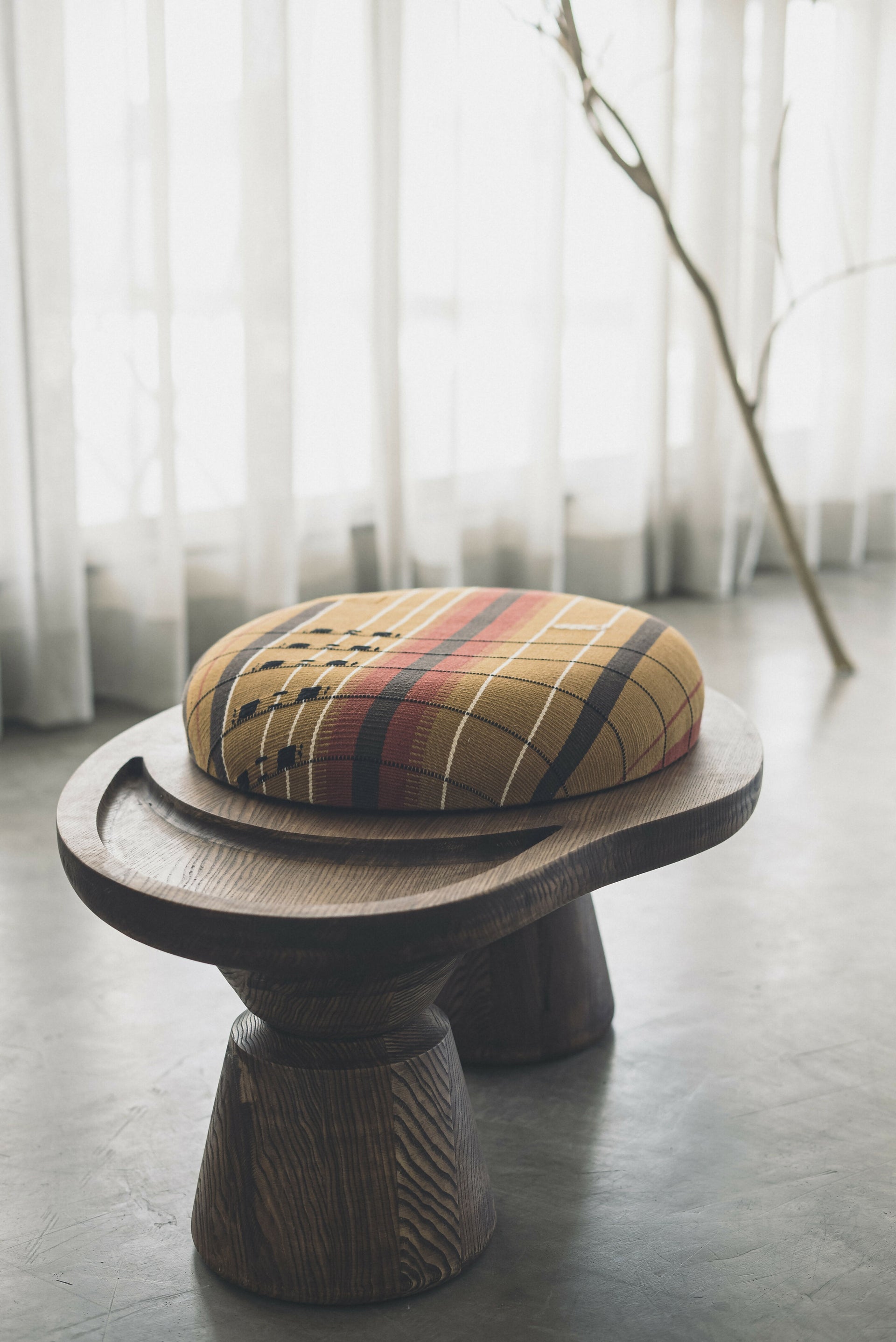A sculptural single-seater ottoman with a curved body, upholstered in mustard color, on a concrete floor,  available  to buy on the-salon.com. SALON curates the finest , unique, handmade pieces from the interior industry's best makers and brands. Shop luxury furniture, lighting, rugs, art, antiques and vintage pieces and accessories from SALON interior designed rooms.