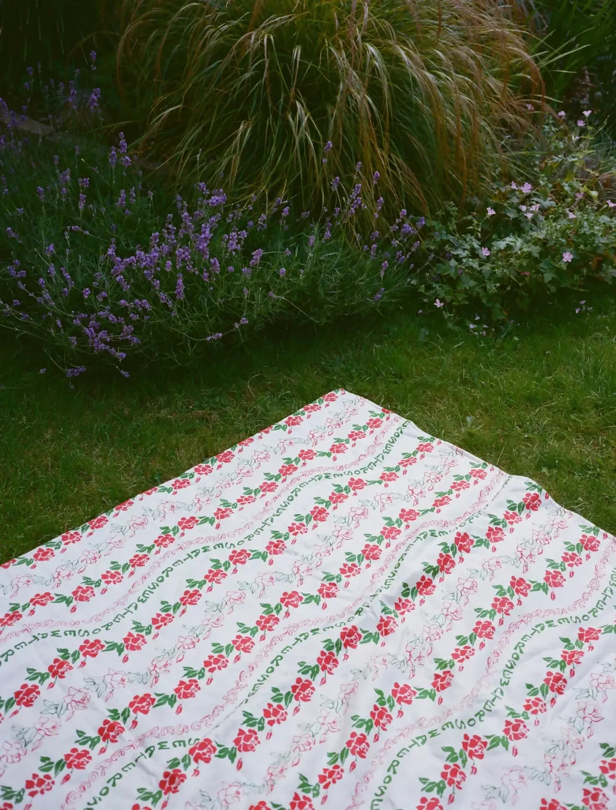 A quilt with a floral pattern featuring roses in red and green colors on a grassy background,  available  to buy on the-salon.com. SALON curates the finest , unique, handmade pieces from the interior industry's best makers and brands. Shop luxury furniture, lighting, rugs, art, antiques and vintage pieces and accessories from SALON interior designed rooms.