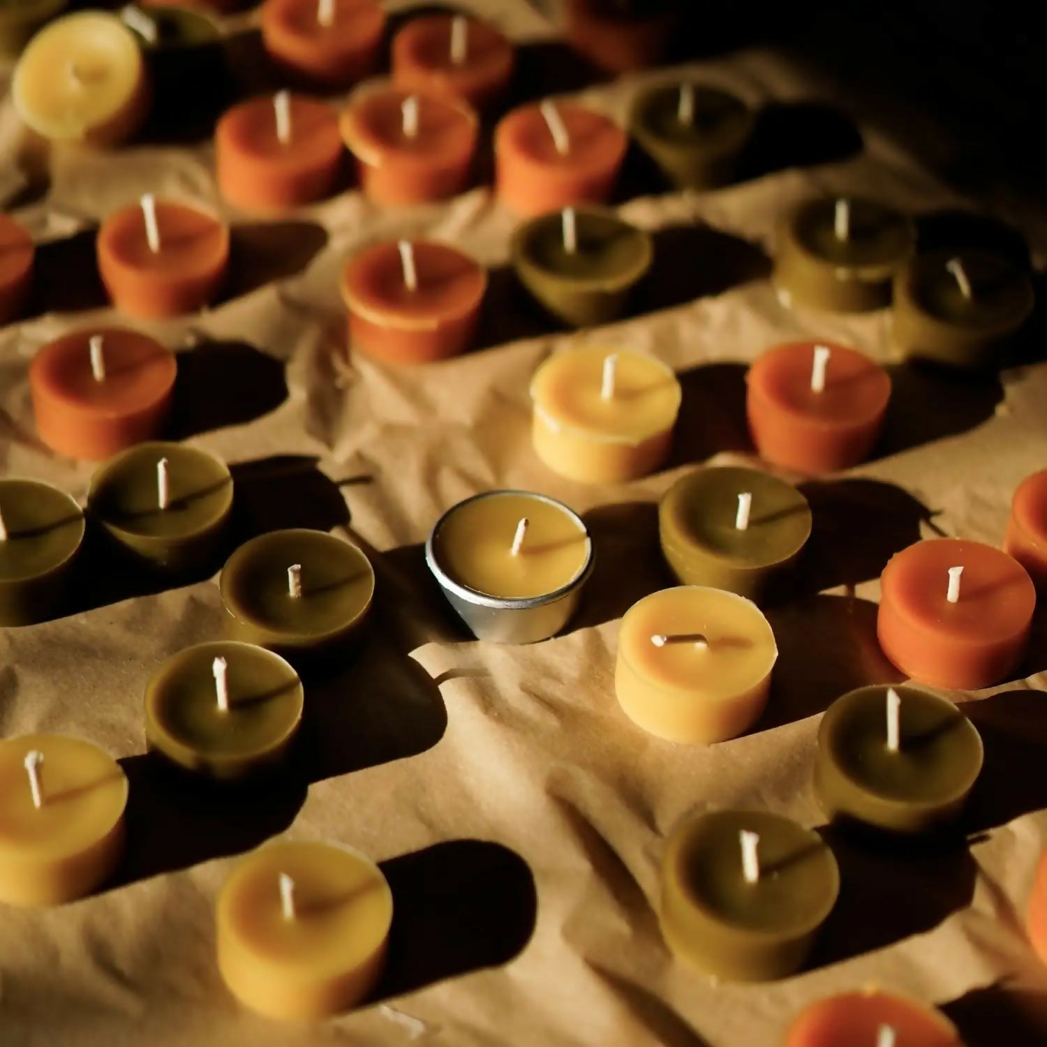 A row of organic beeswax tealights arranged on a white surface with a tealight holder to the side, available  to buy on the-salon.com. SALON curates the finest , unique, handmade pieces from the interior industry's best makers and brands. Shop luxury furniture, lighting, rugs, art, antiques and vintage pieces and accessories from SALON interior designed rooms.